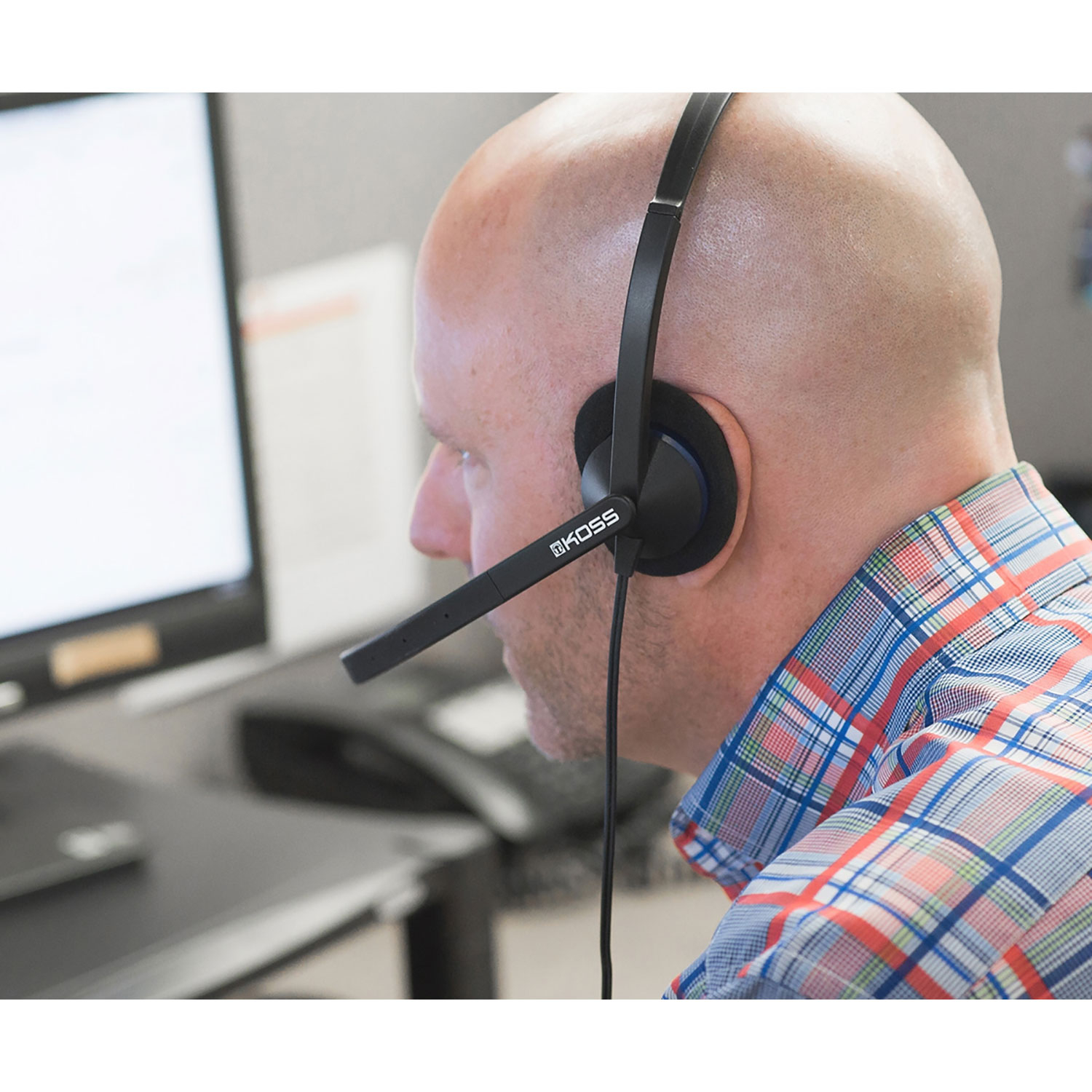 Łysy mężczyzna w zestawie słuchawkowym, patrzący na ekran komputera. Biuro.