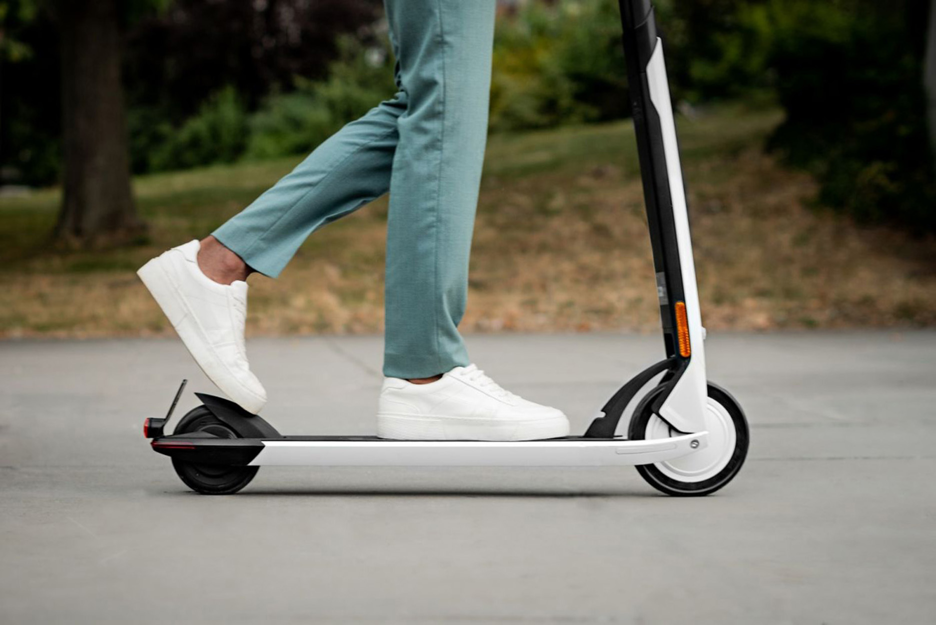 Eine Person auf einem Elektroroller auf einem befestigten Weg. Der Roller ist weiß und schwarz.