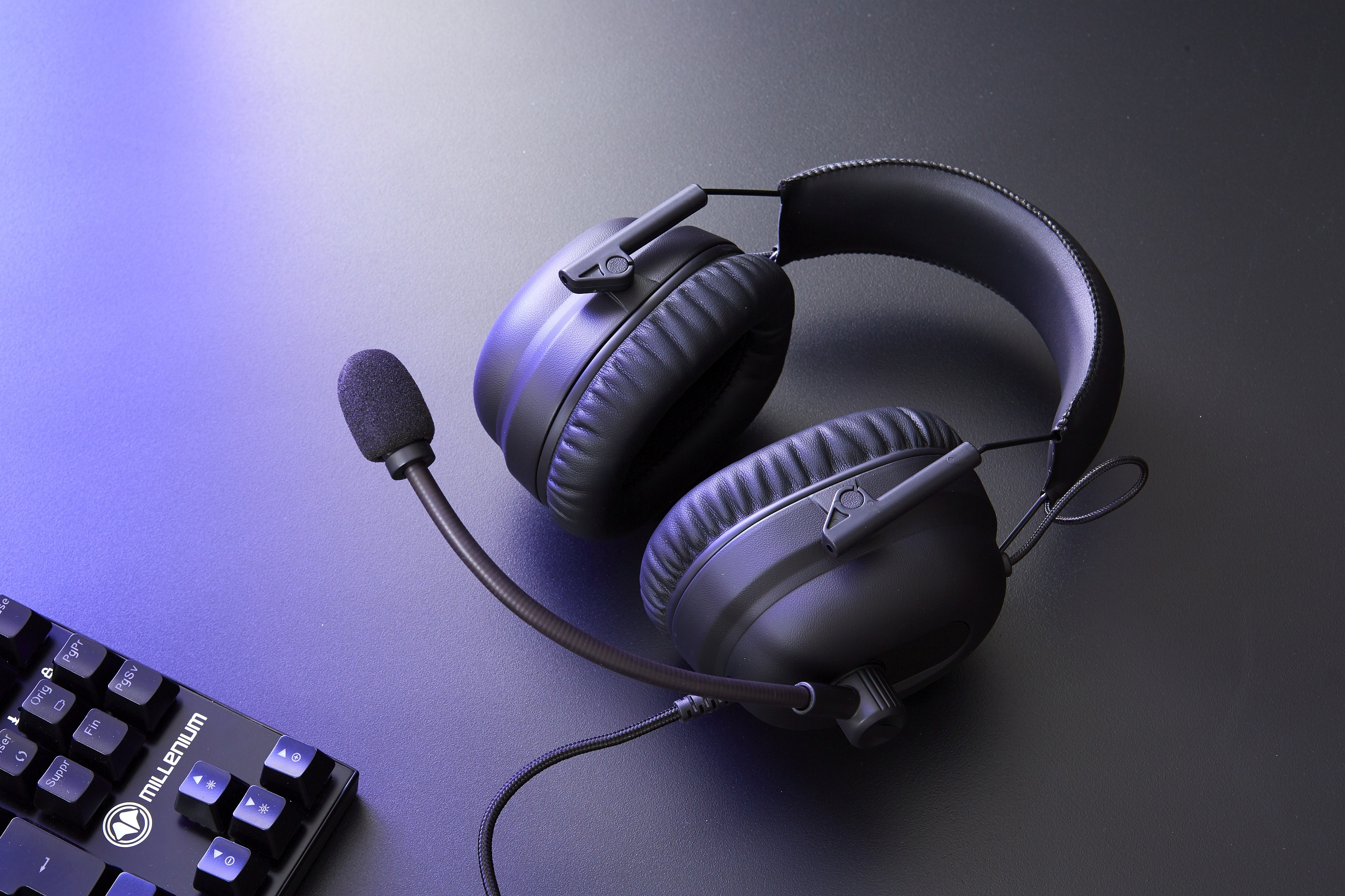 Auriculares gaming negros con micrófono, sobre una superficie oscura con teclado parcialmente visible.