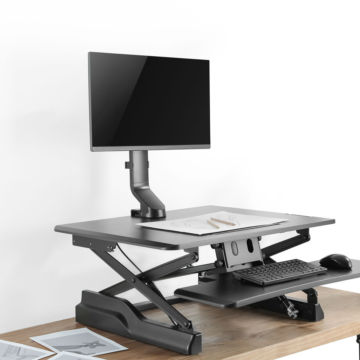 Statafel met een monitor, toetsenbord en muis. Er is een tekening en een houten tafel.