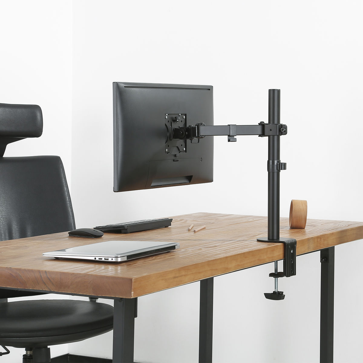 Monitor op een bureau gemonteerd met een monitorarm. Het bureau is van hout, de achtergrond is wit.