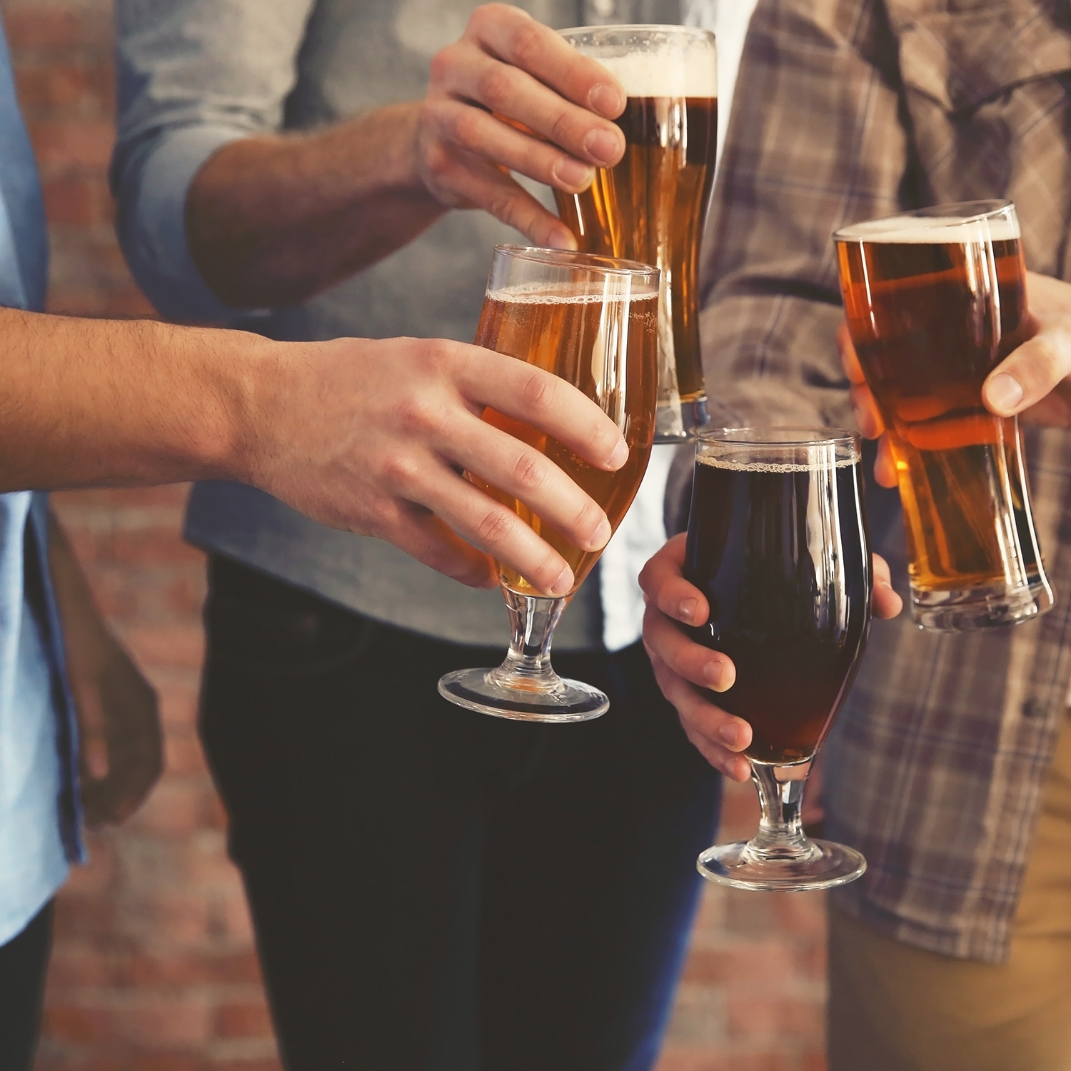 Tre persone che tengono bicchieri di birra. Le birre variano per colore e schiuma. Primo piano.