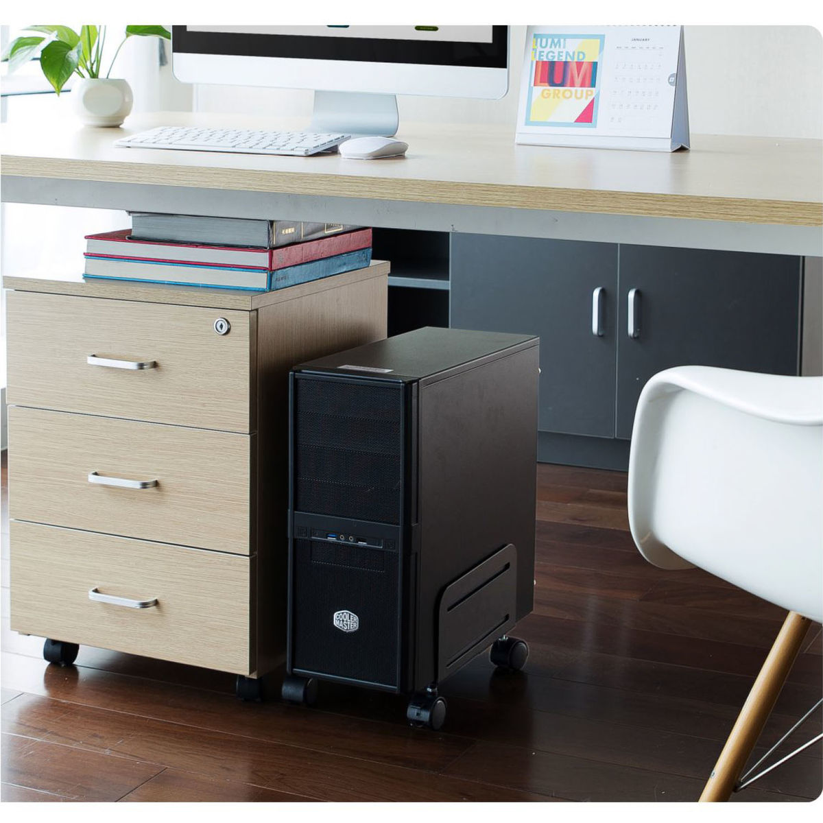 Un computer tower, una scrivania con monitor e un mobile con cassetti.