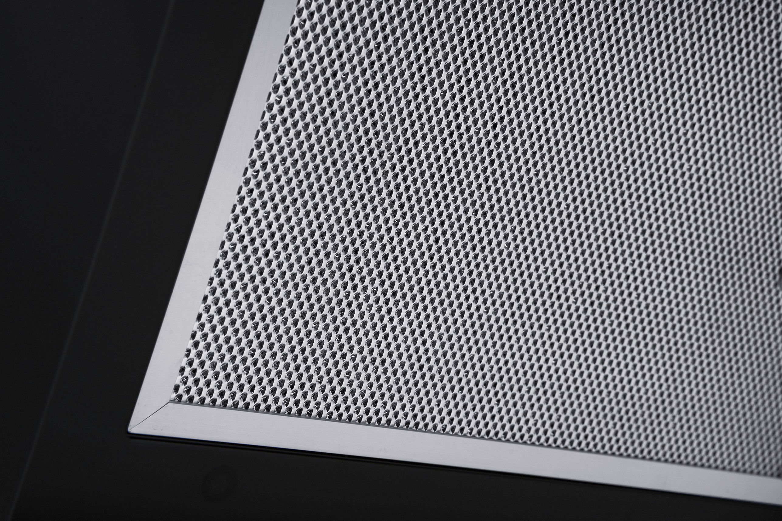 Primo piano di un filtro metallico perforato su una cappa nera.
