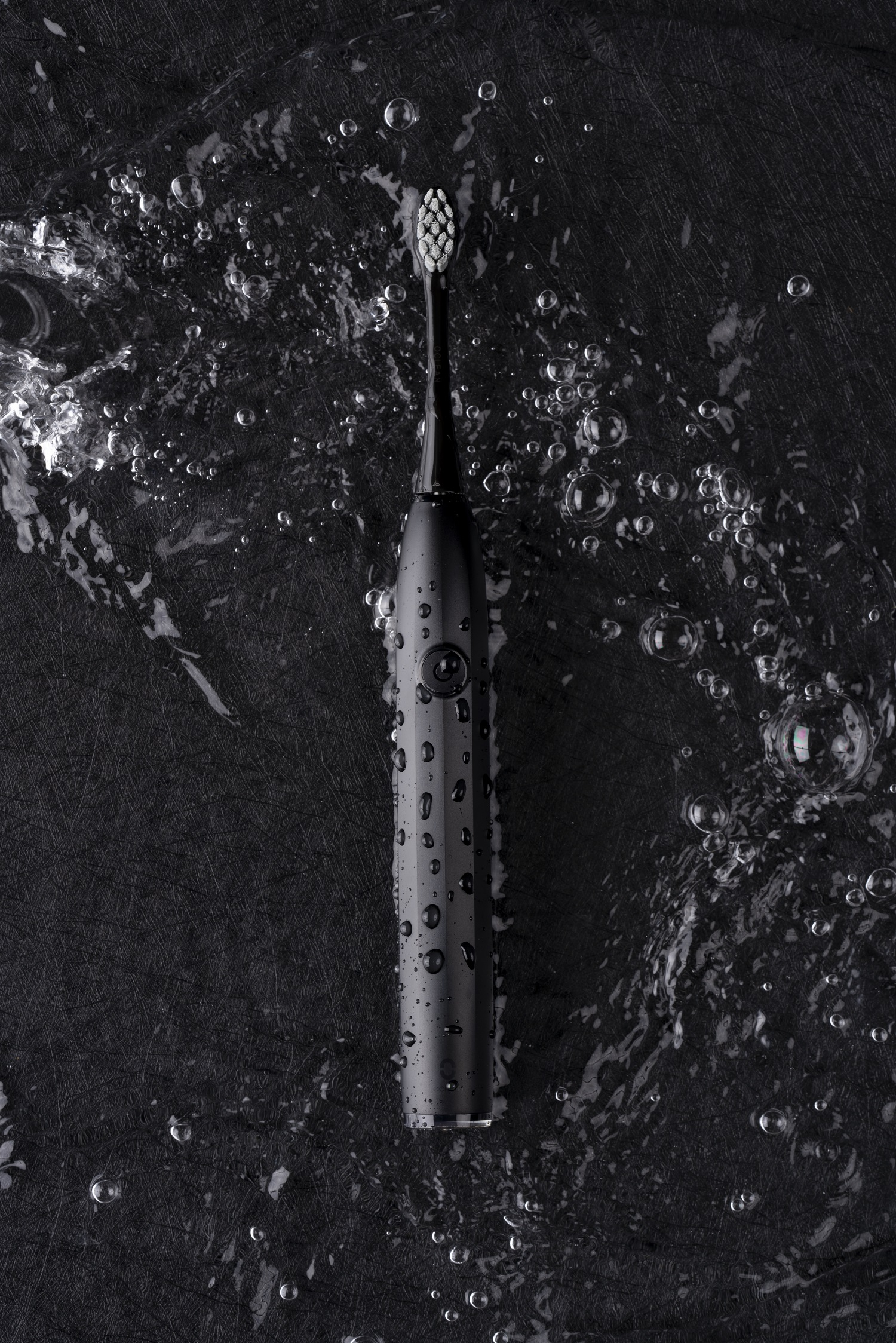 Schwarze elektrische Zahnbürste im Wasser. Wassertropfen sind sichtbar. Der Bürstenkopf ist weiß.