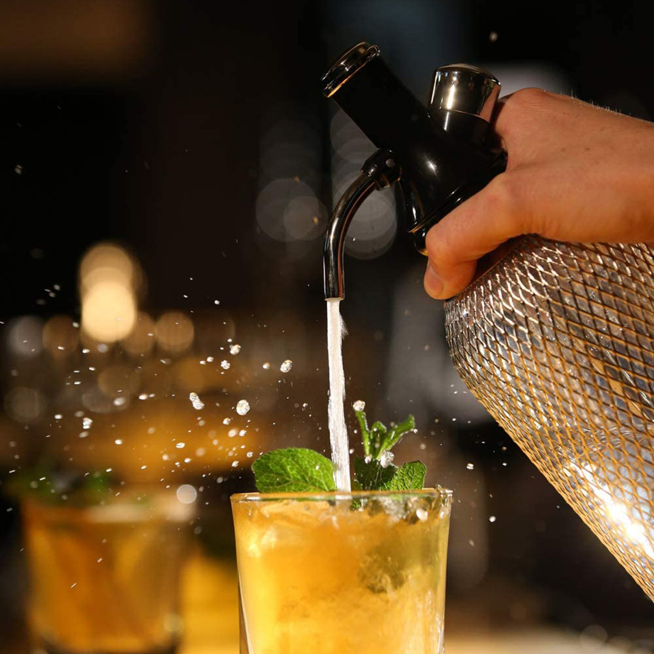 Ein Barkeeper gießt einen Cocktail mit Minzblättern in ein Glas. Blasen sind sichtbar, was eine erfrischende Szene erzeugt.