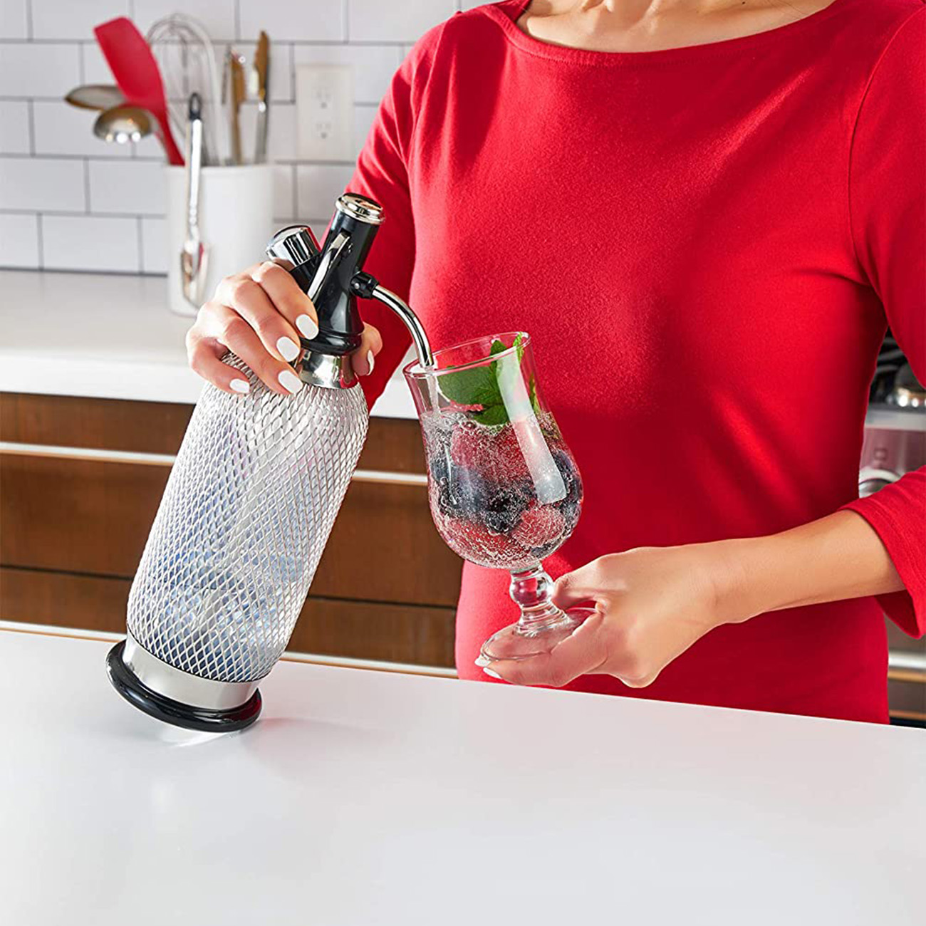 Eine Frau bereitet ein Getränk mit einem Sodabereiter und Beeren zu.