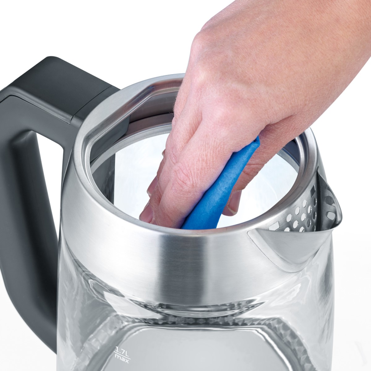 Dłoń czyszcząca szklany czajnik niebieską gąbką, zbliżenie.