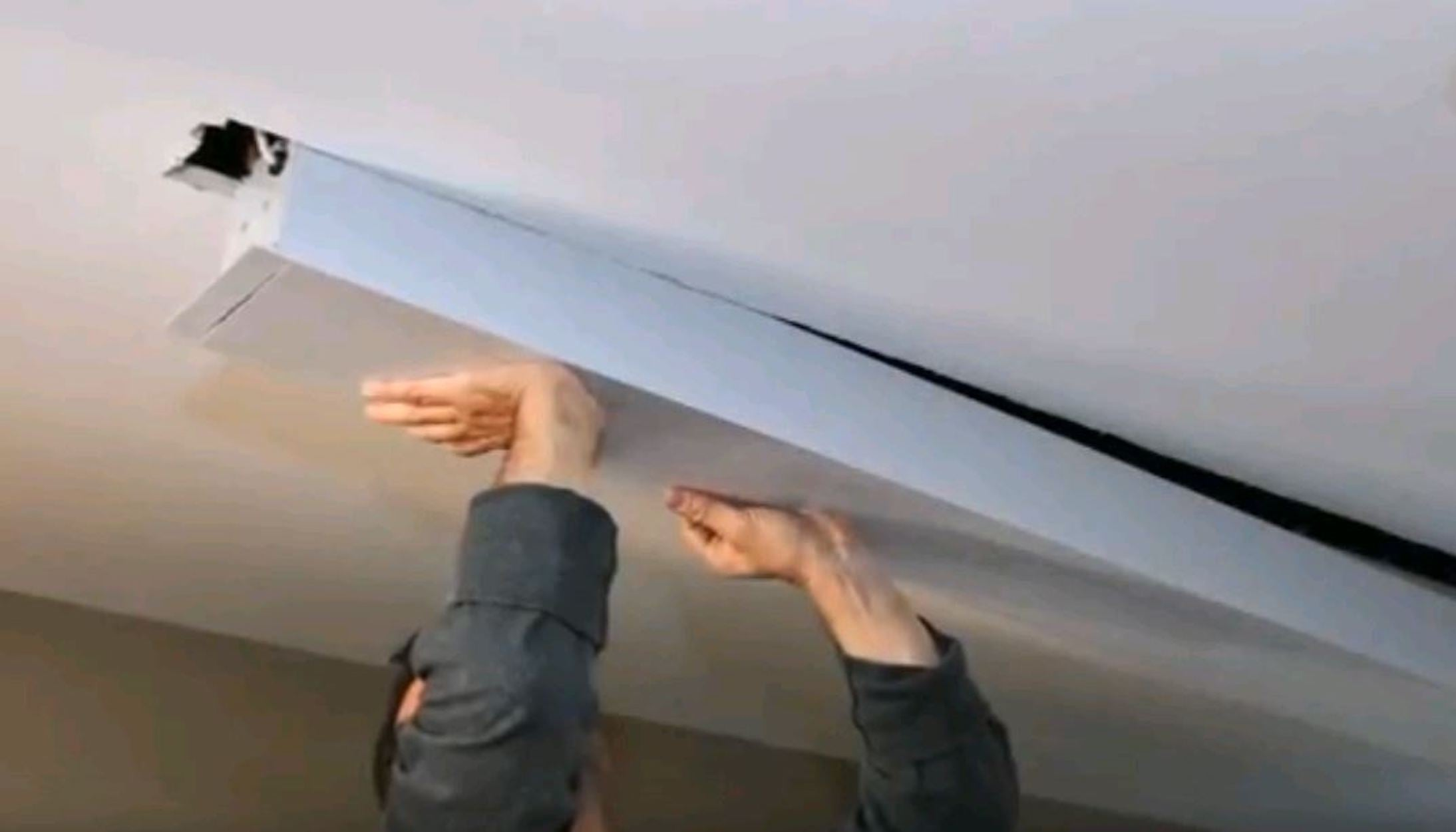 Persona che installa un pannello rettangolare bianco sul soffitto. Mani visibili, che tengono il pannello.