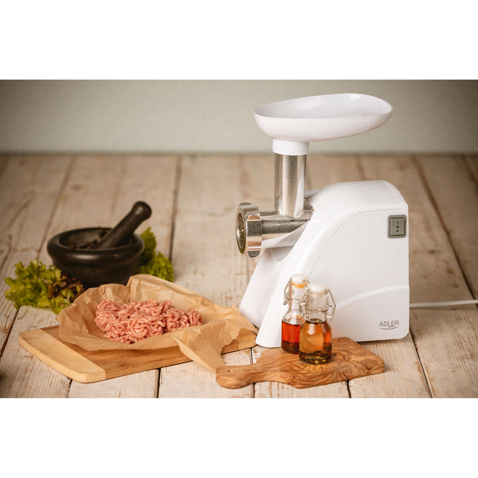 Biała maszynka do mięsa, czarny moździerz i tłuczek oraz małe butelki oleju na drewnianym stole.