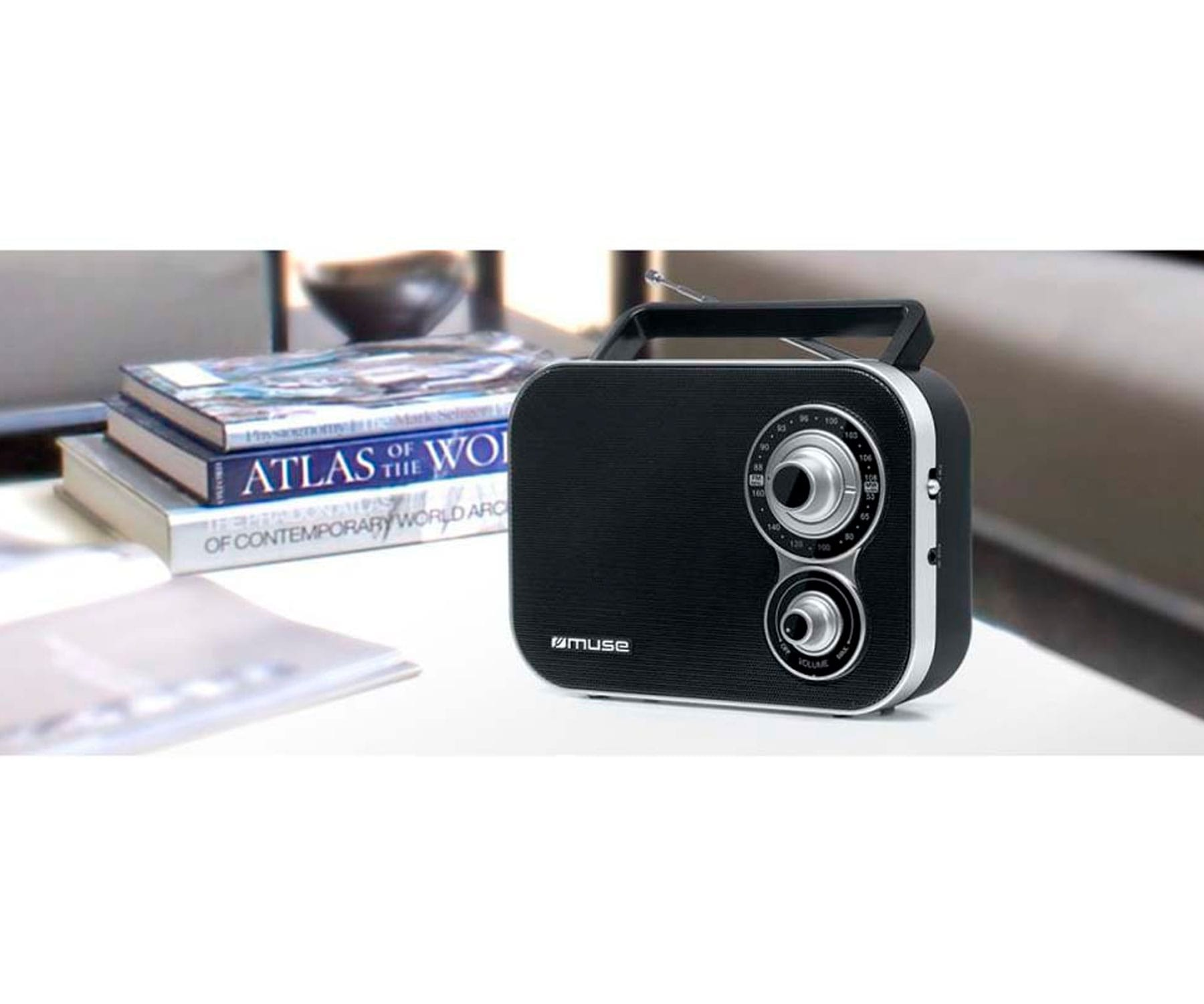 Czarny radio z srebrnymi pokrętłami i przyciskami na białej powierzchni, z książkami w tle.