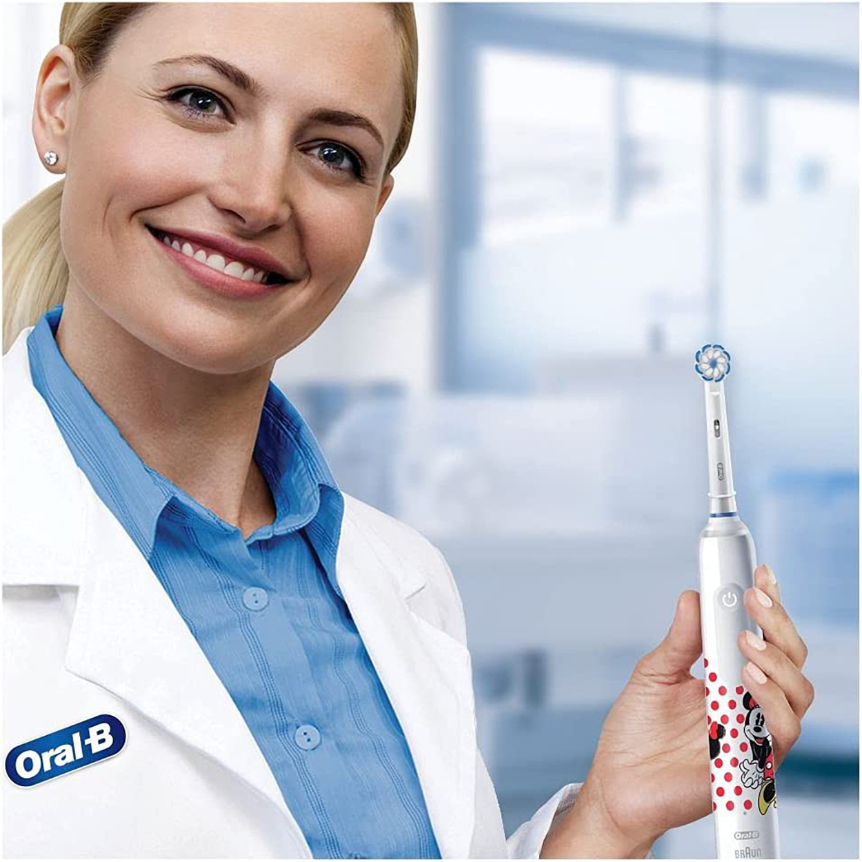 Una donna in camice sorride, tenendo in mano uno spazzolino elettrico Oral-B con un design di Topolino.