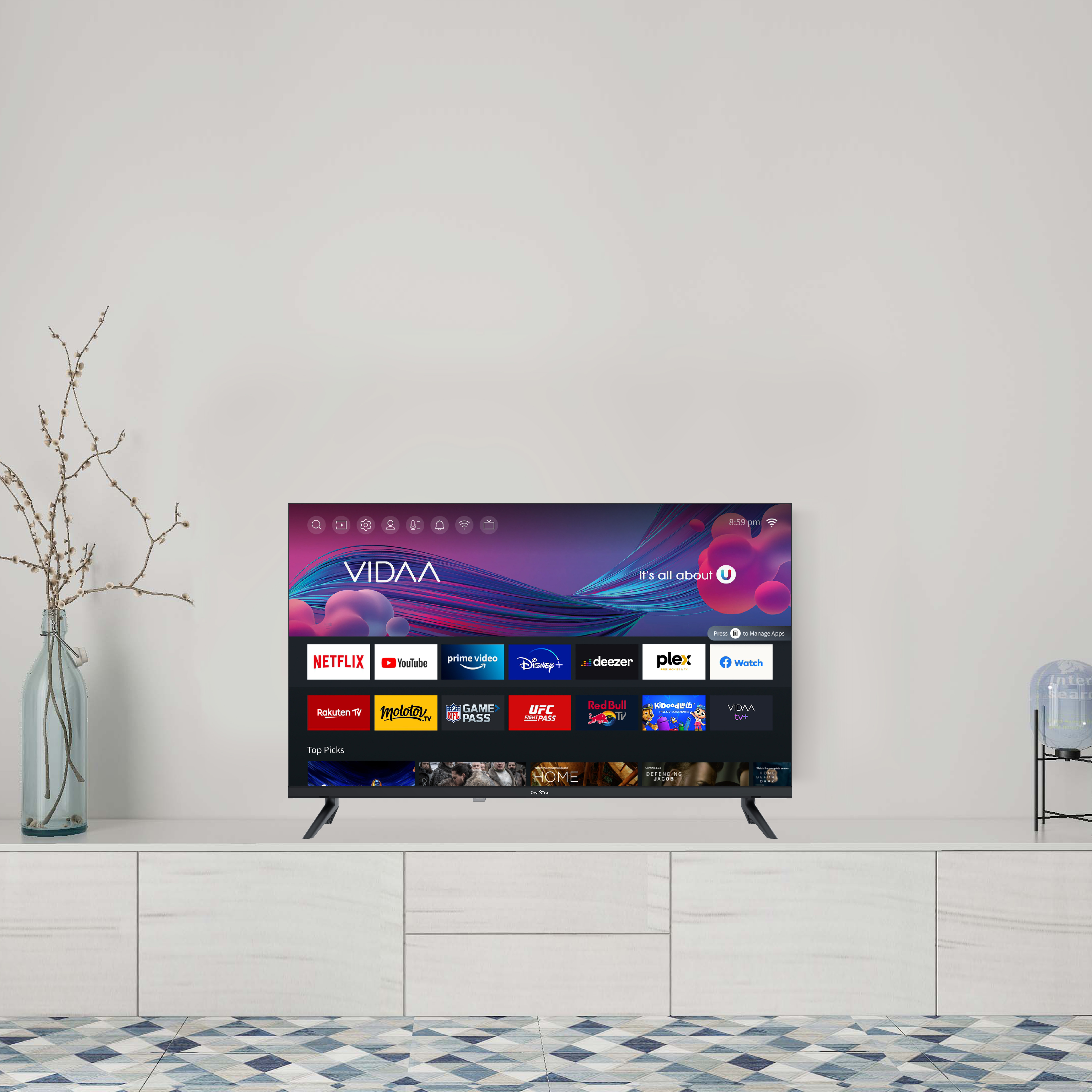 Telewizor na białej szafce, aplikacje na ekranie. Wazon z gałęziami po lewej.