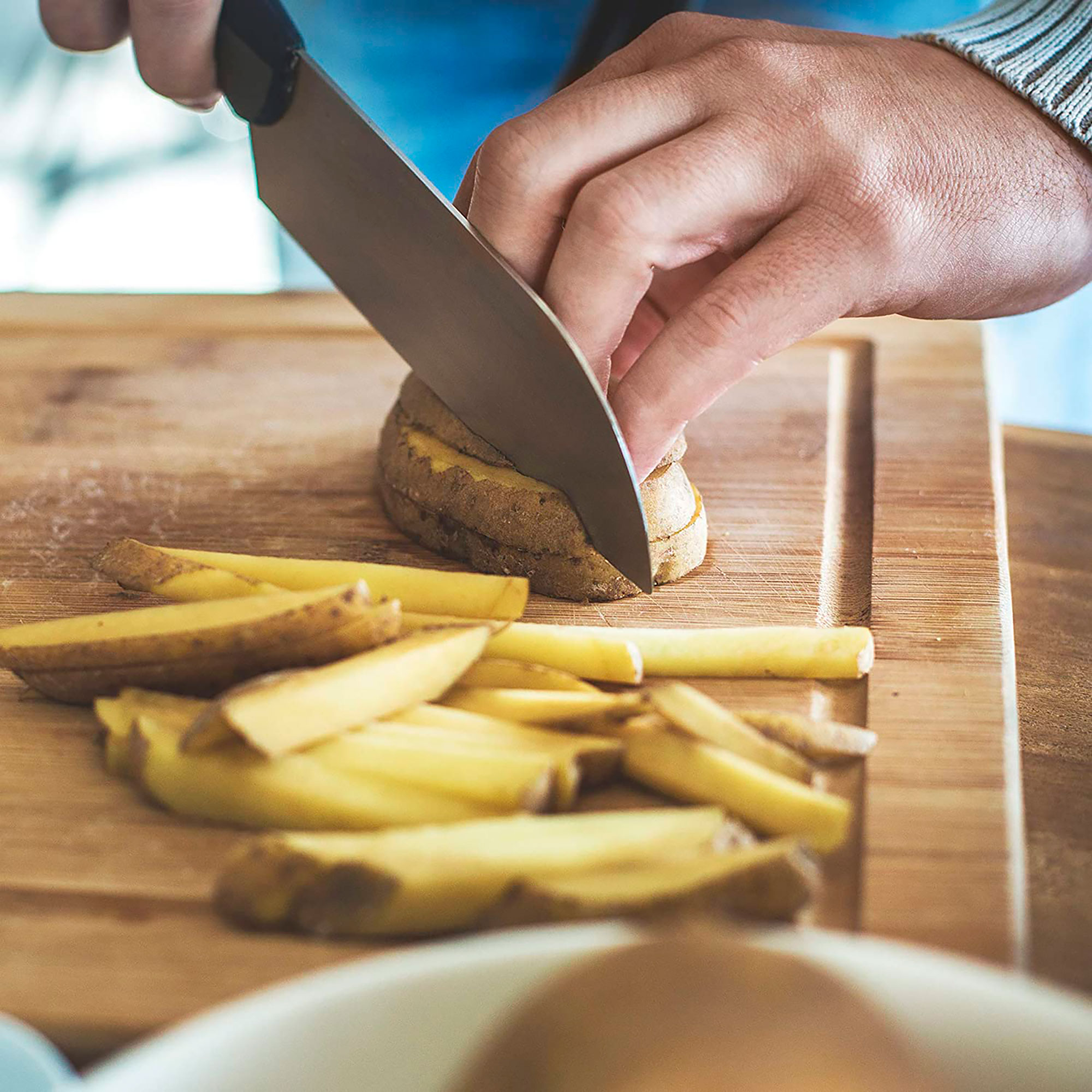 Osoba kroi ziemniaka na drewnianej desce. Kilka plasterków ziemniaka jest widocznych.