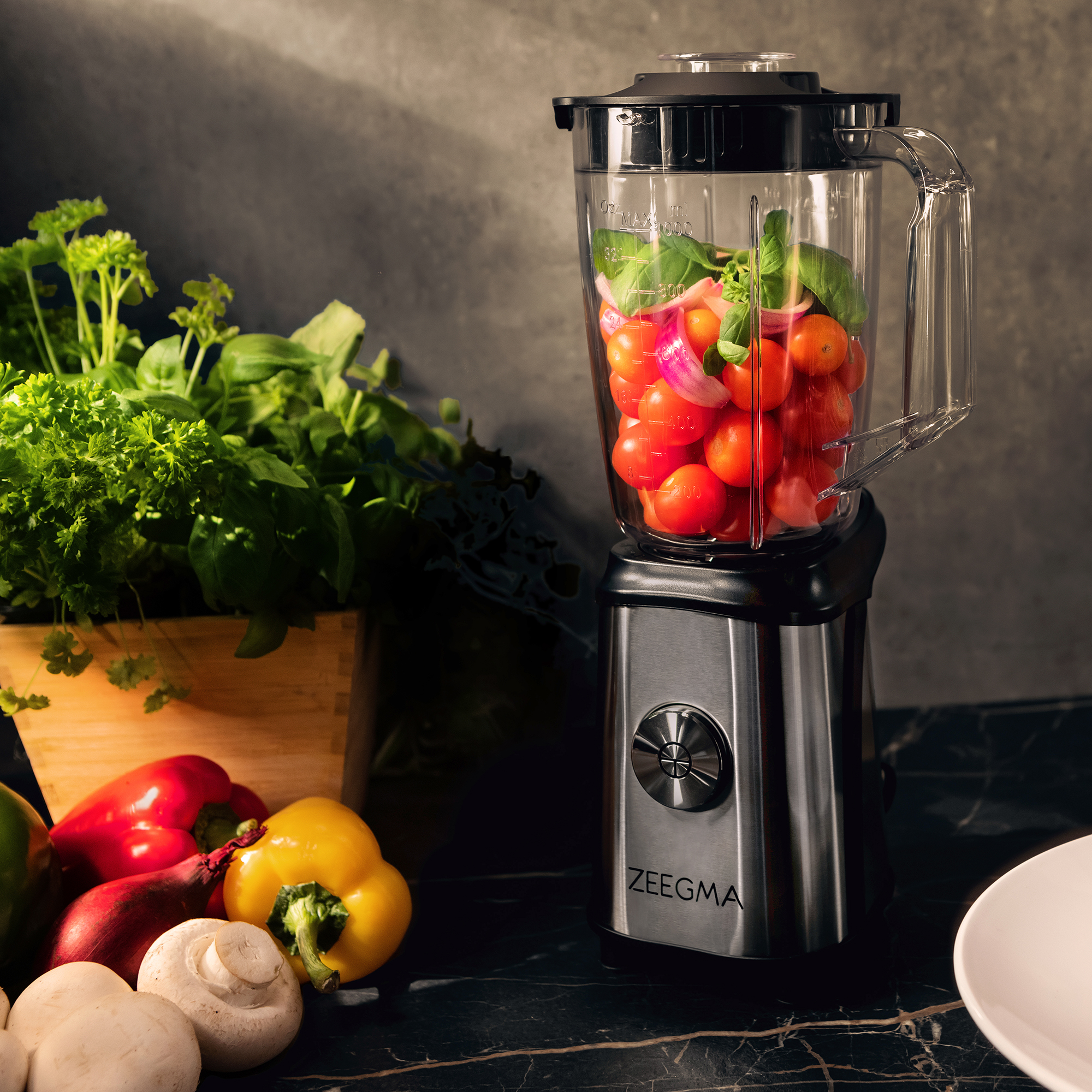 Blender z pomidorami i cebulą w środku. Otoczony warzywami. Ciemny blat.