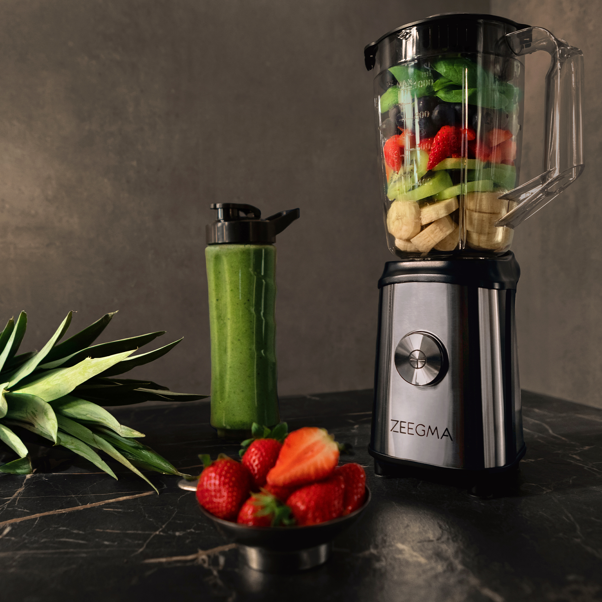 Blender z owocami, koktajl w butelce, truskawki i ananas na stole.