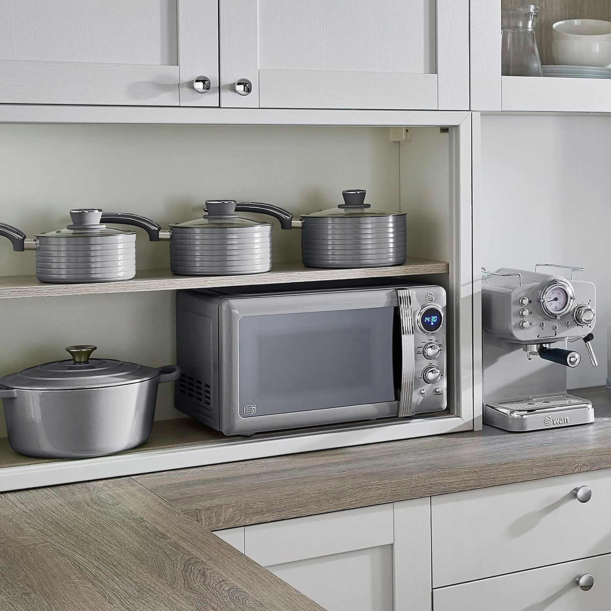 Küchenszene mit grauer Mikrowelle, Töpfen und Kaffeemaschine. Alle sind in Schränken platziert.