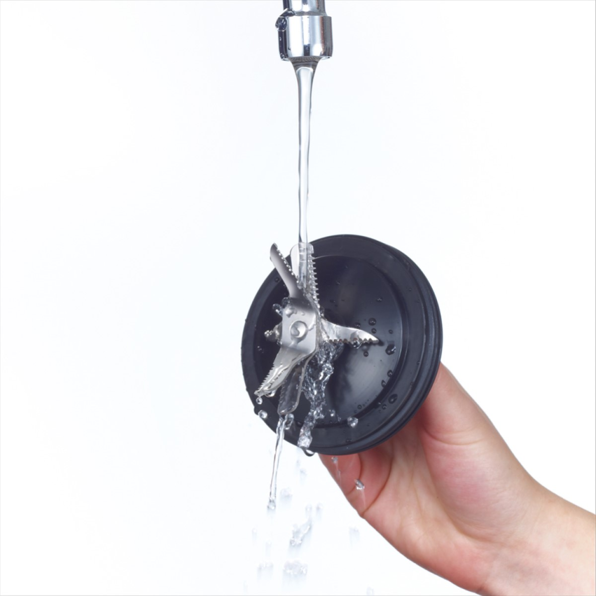 A hand holding a black blender blade attachment under running water. The attachment is black and metallic.