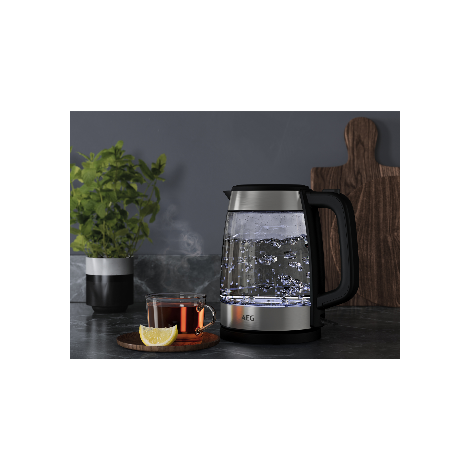 Ein elektrischer Glaskessel mit kochendem Wasser und Dampf. Eine Tasse Tee und Zitronenscheibe sind im Bild.