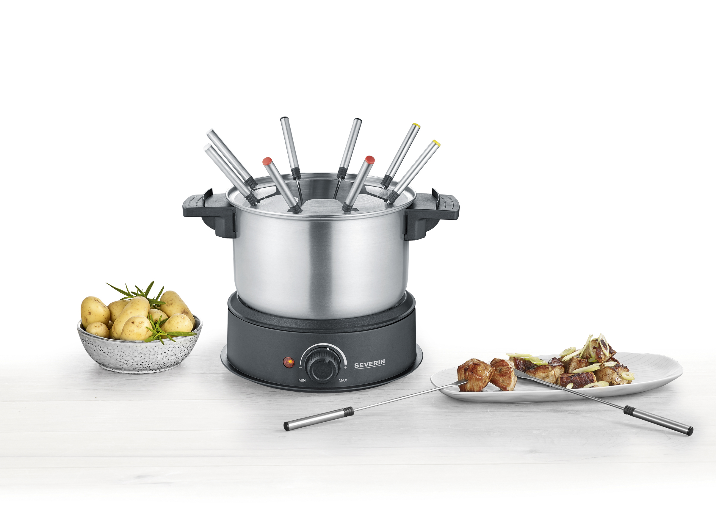 A fondue set with a pot, forks and food on a plate. Potatoes and rosemary in a bowl.