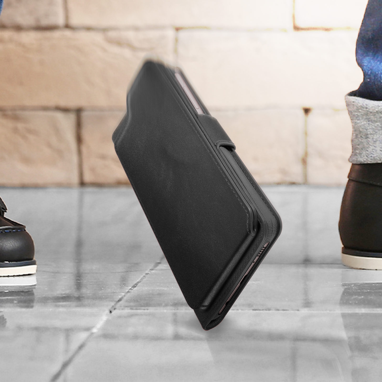 Custodia nera per telefono, angolata, su superficie riflettente. Parti delle gambe di una persona sullo sfondo.
