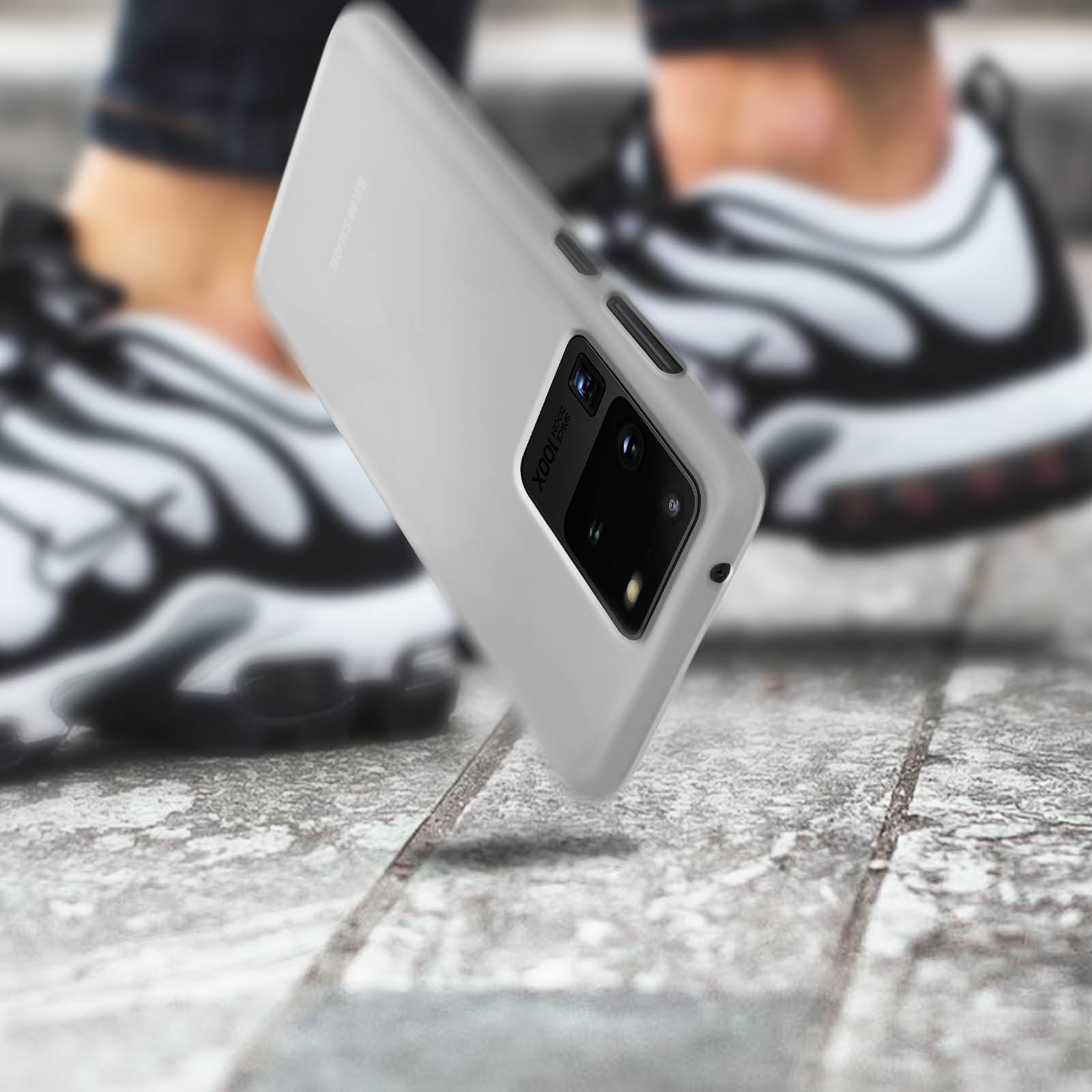 Graue Handyhülle für Samsung, in der Hand gehalten, mit verschwommenem Hintergrund von Schuhen.