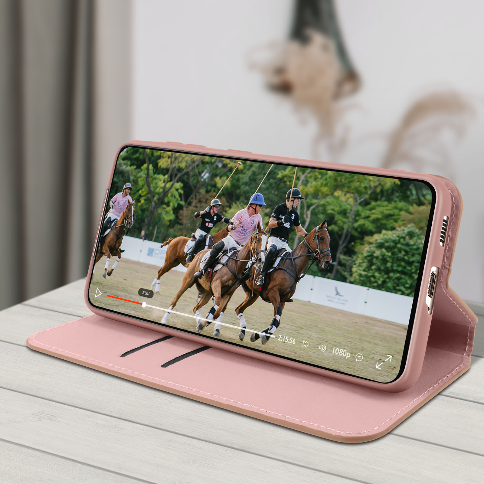 Uno smartphone in una custodia rosa che mostra un video di una partita di polo, aperto su un tavolo di legno.