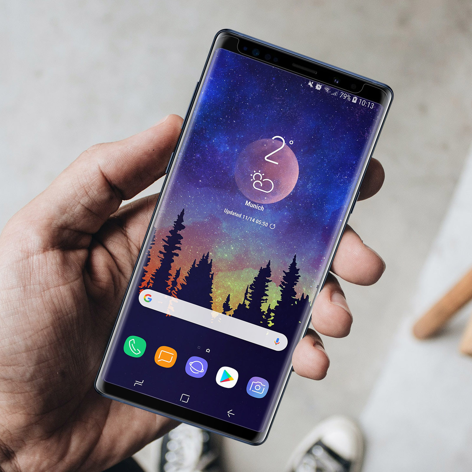 Une main tient un smartphone avec un fond d'écran de ciel étoilé et des icônes d'applications.