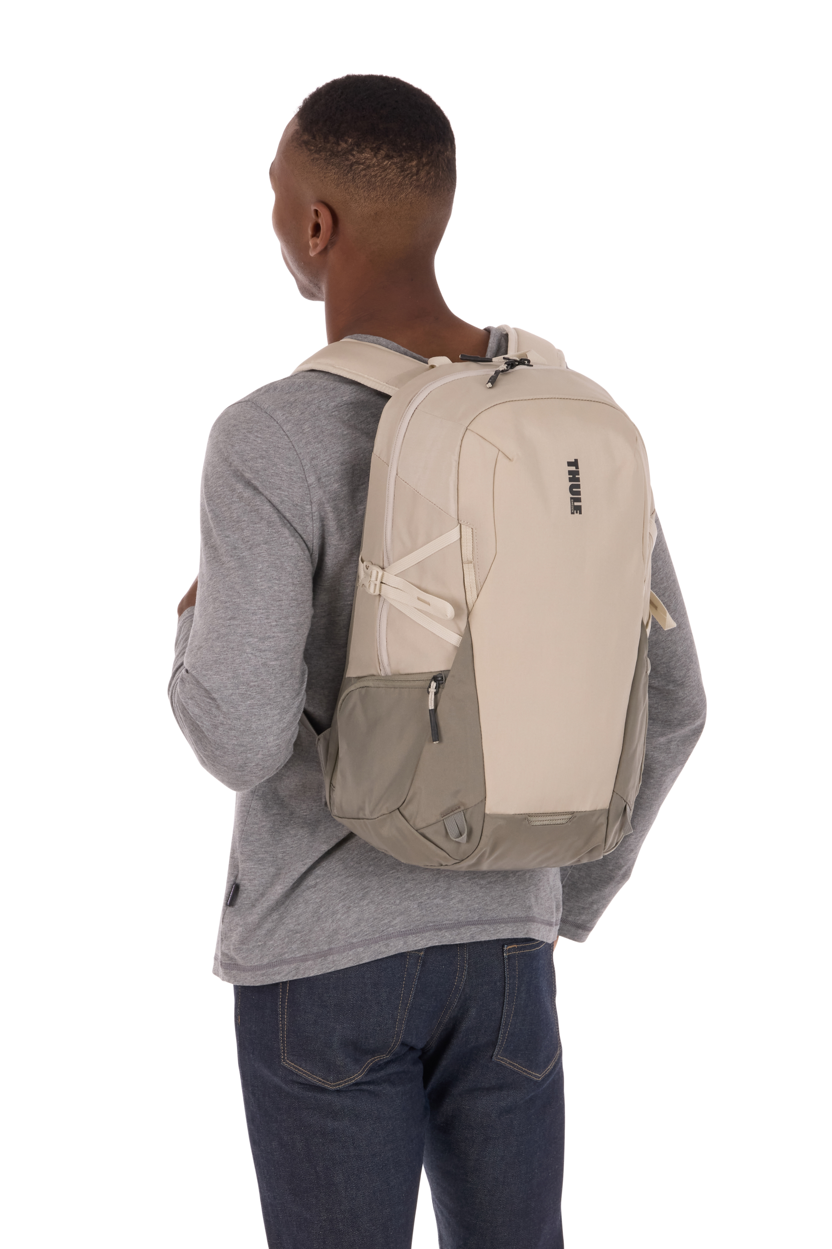 Mann in grauem Hemd und Jeans mit beigem und grauem Thule-Rucksack.