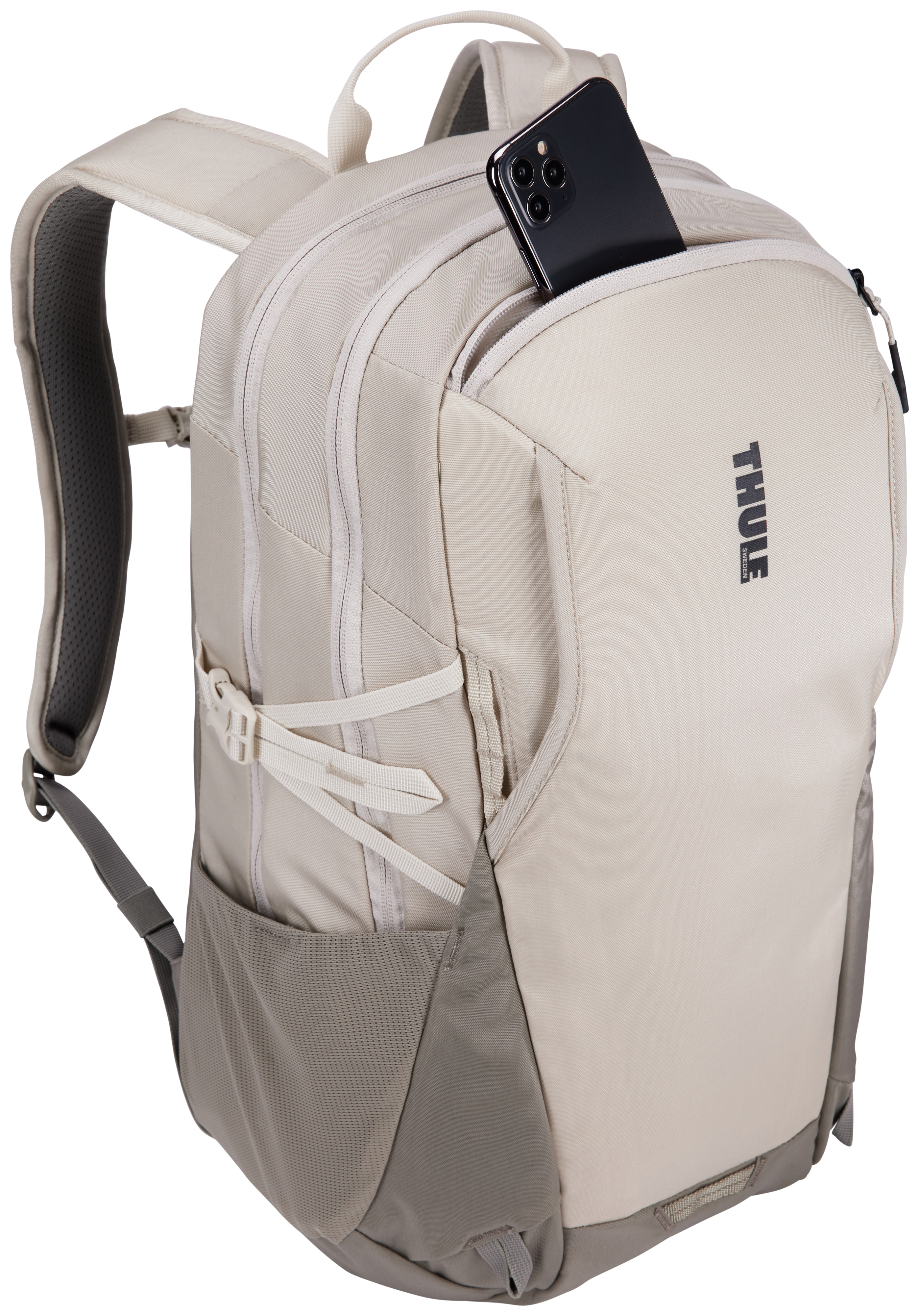 Beiger Rucksack mit Telefon in der Vordertasche. Thule-Logo sichtbar. Weiße Gurte und graue Akzente.