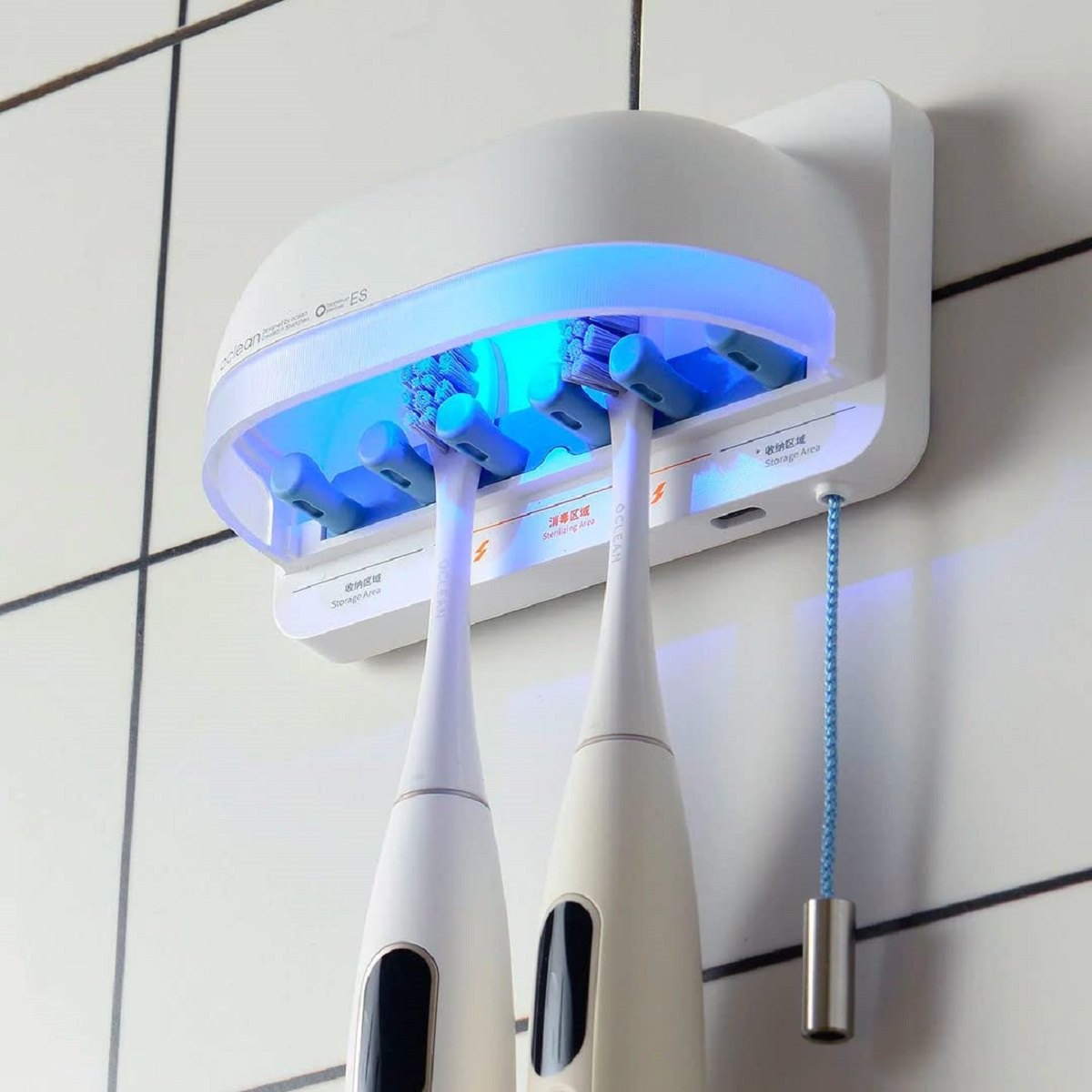 Weißer Zahnbürsten-Sanitizer mit zwei Zahnbürsten, blaues Licht. An einer gefliesten Wand montiert.
