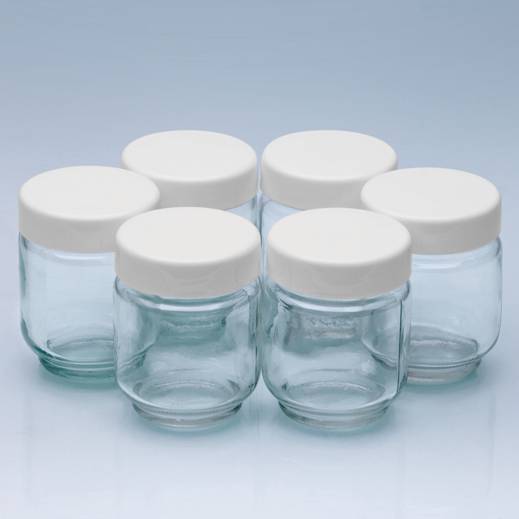 Sześć małych szklanych słoików z białymi pokrywkami ułożonych w okrąg.