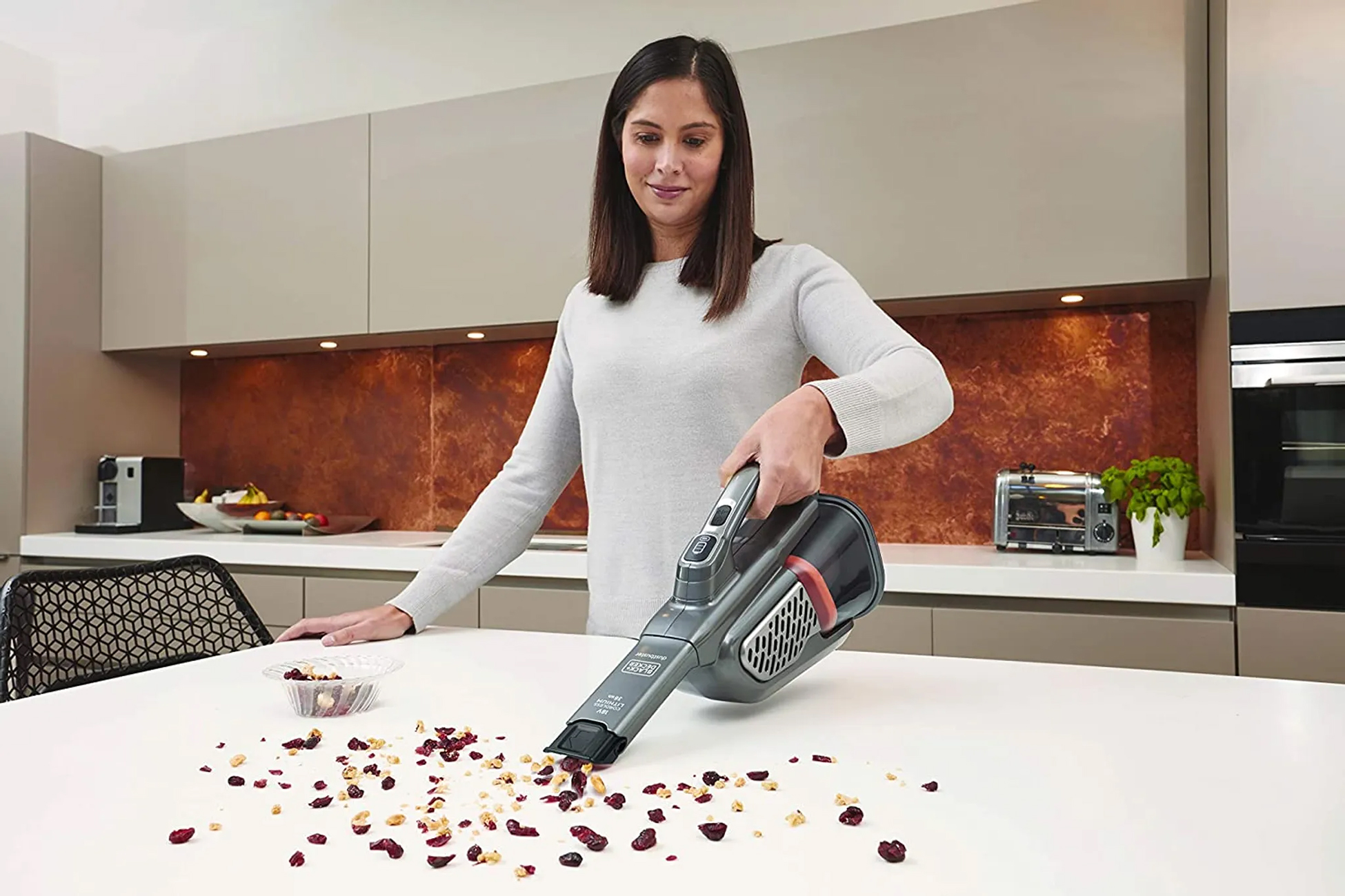 Woman using a handheld vacuum to clean a white countertop with spilled food.