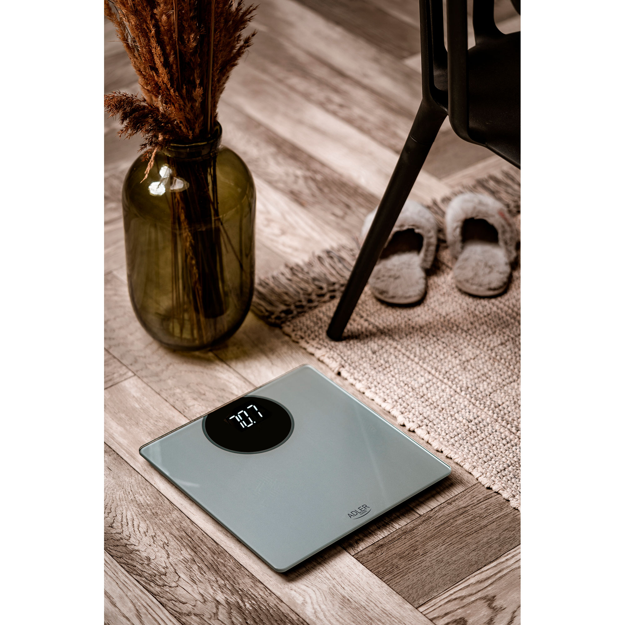 Waga cyfrowa z wyświetlaczem 70.7, wazon z suszonymi kwiatami, kapcie i krzesło.