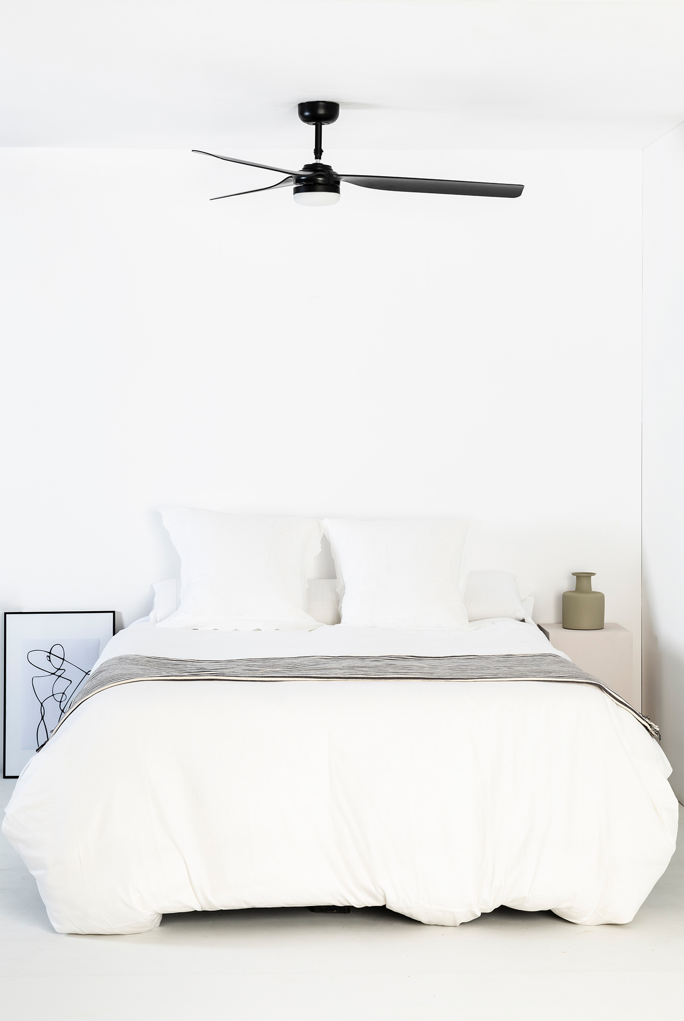Schlafzimmer mit weißen Wänden und Bett. Schwarzer Deckenventilator.