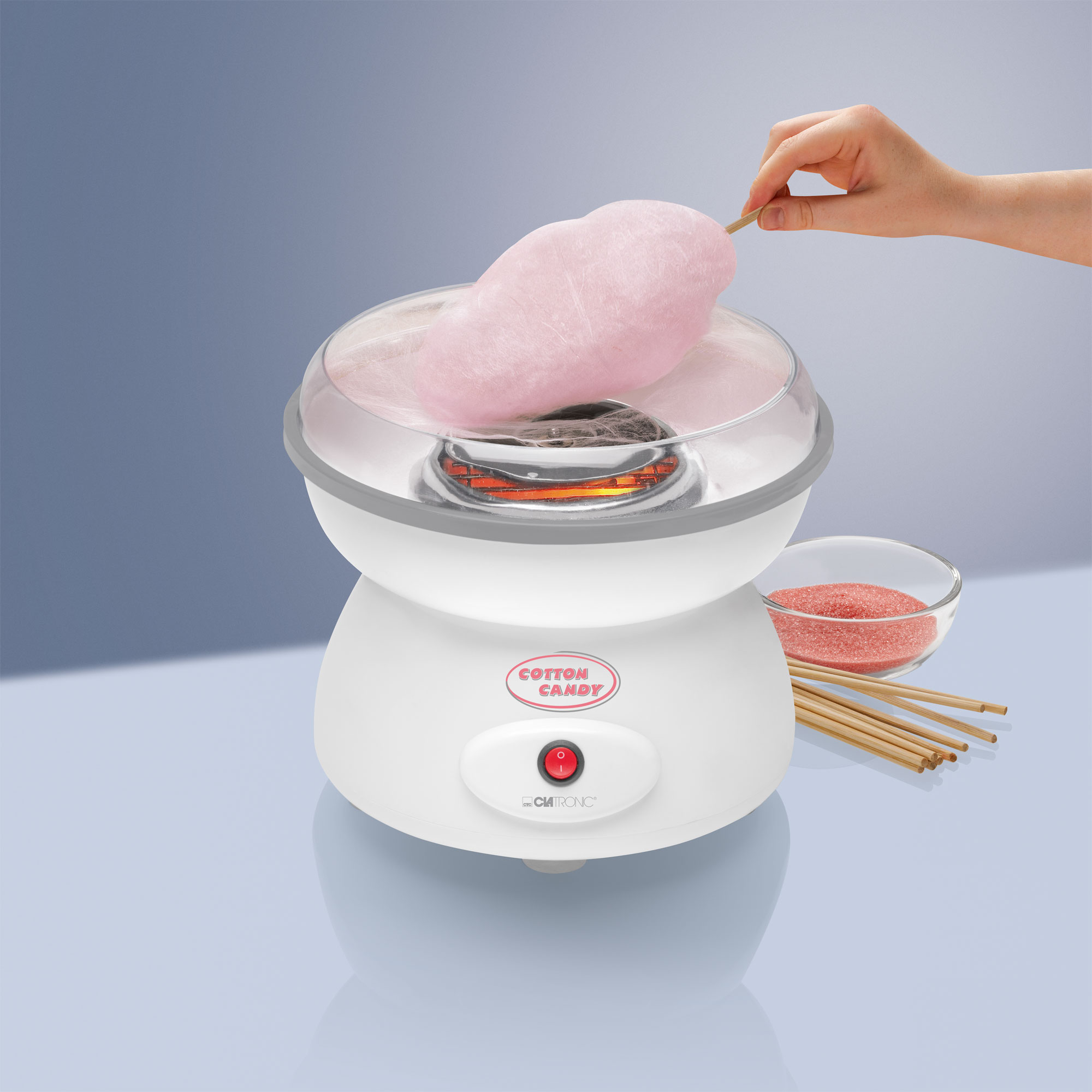Una máquina de algodón de azúcar con algodón de azúcar rosa. Un tazón de azúcar rosa al lado.
