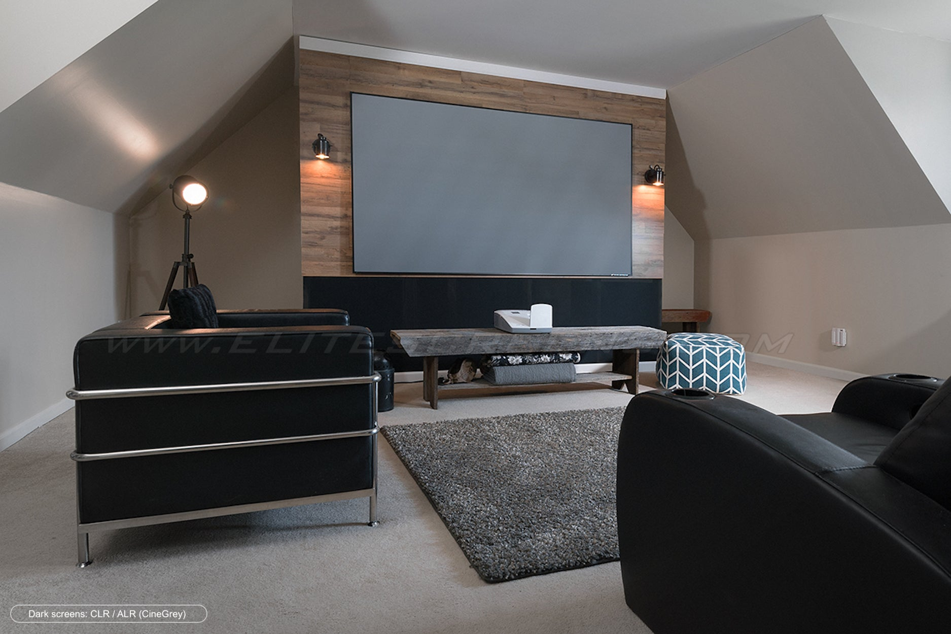 Heimkino-Setup auf dem Dachboden mit großem Bildschirm, schwarzen Sitzgelegenheiten und Holzverkleidung.