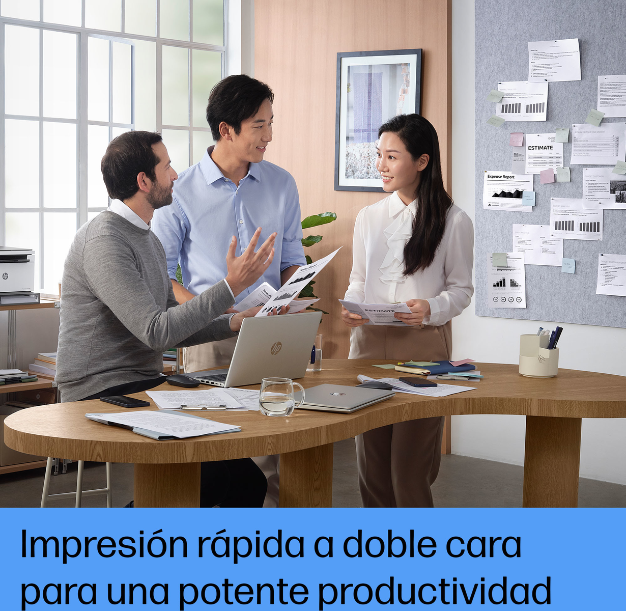 Trzy osoby współpracują przy drewnianym stole, omawiając dokumenty. Widoczna drukarka i dokumenty.