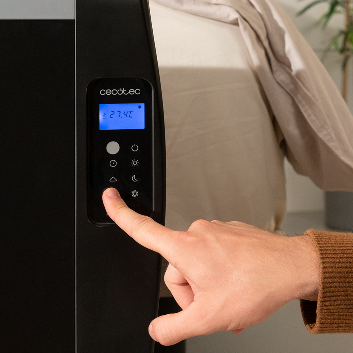 Ręka osoby naciskająca przycisk na czarnym wyświetlaczu grzejnika pokazującym 27,4°C.