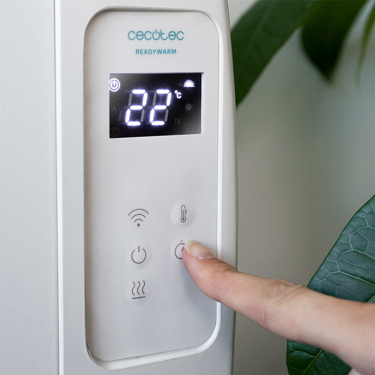 Ręka naciska przycisk na białym urządzeniu. Wyświetlacz cyfrowy pokazuje '22°C'.