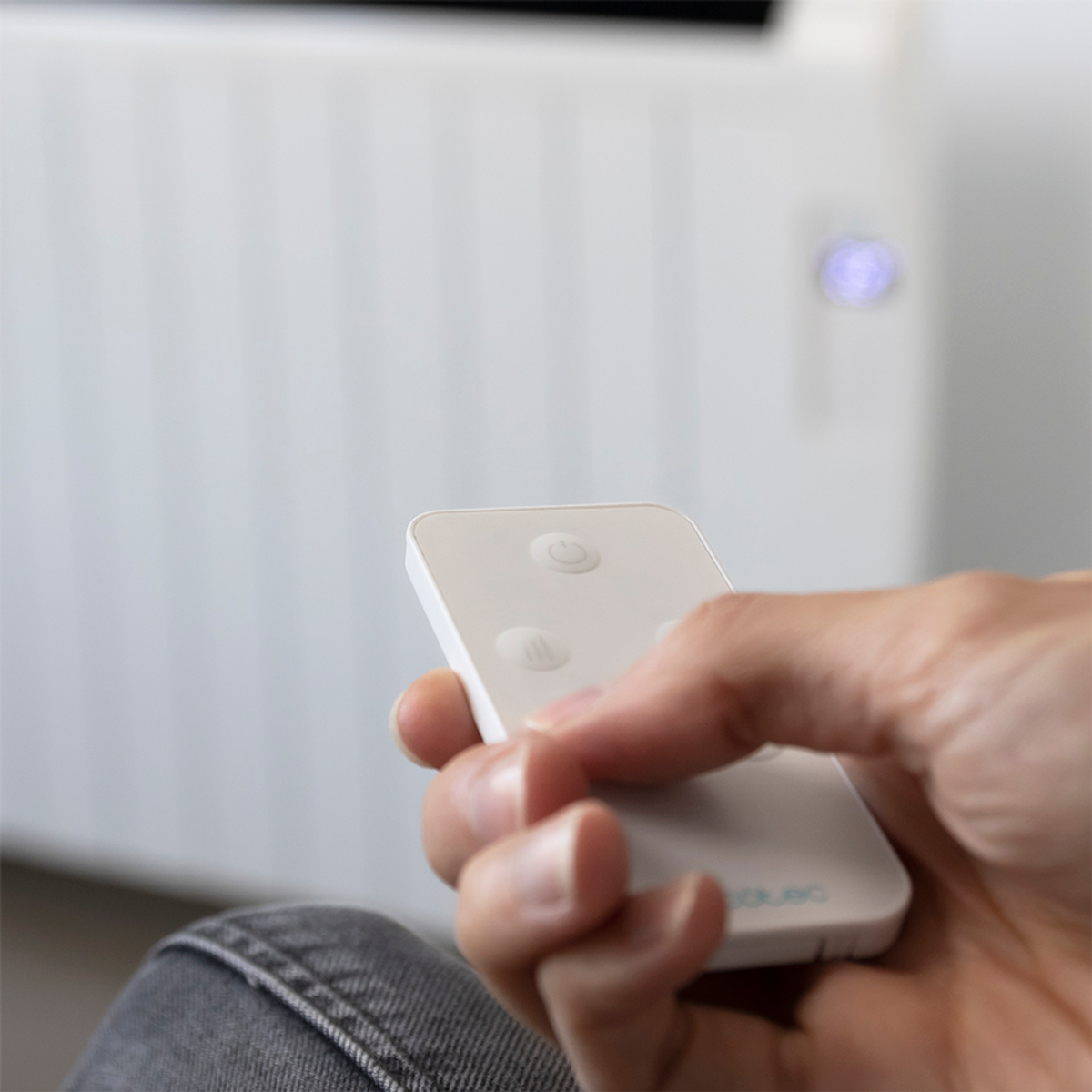 Dłoń osoby trzymająca biały pilot przed białym grzejnikiem. Rozmyte tło.