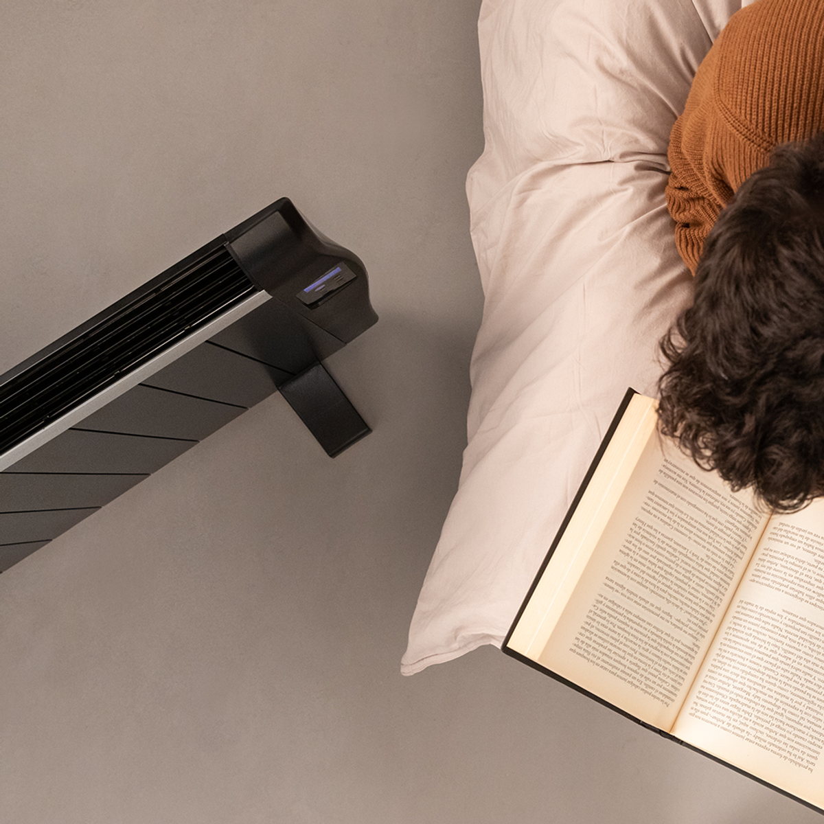 Osoba czyta książkę przy łóżku. Grzejnik w tle.