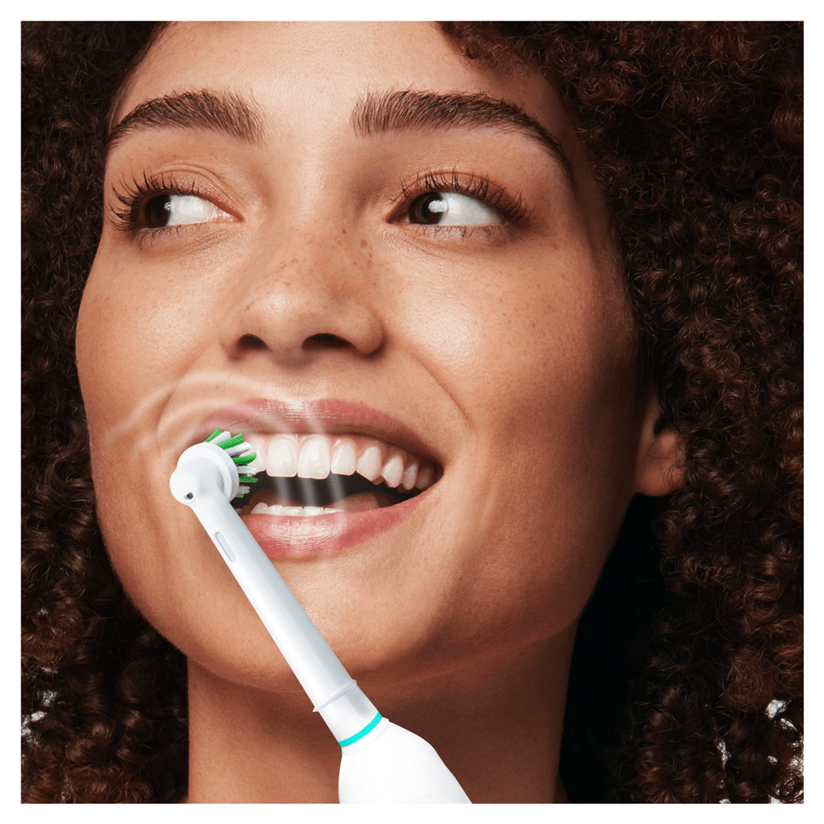 Una mujer se cepilla los dientes con un cepillo eléctrico. Se ve espuma y vapor.