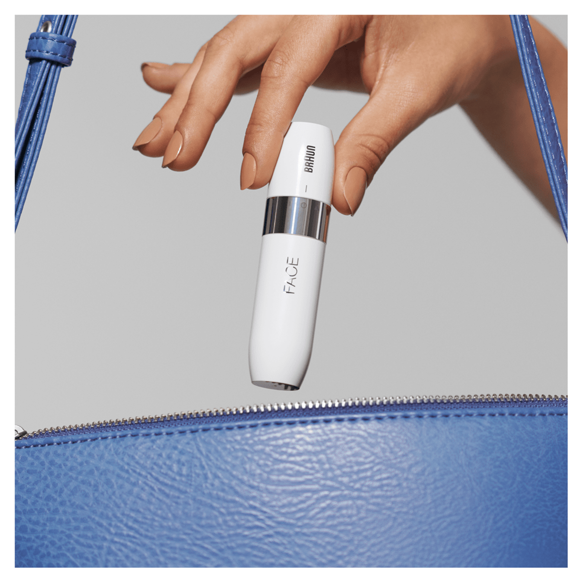 Mano che tiene un dispositivo Braun Face bianco, sopra una borsa blu.