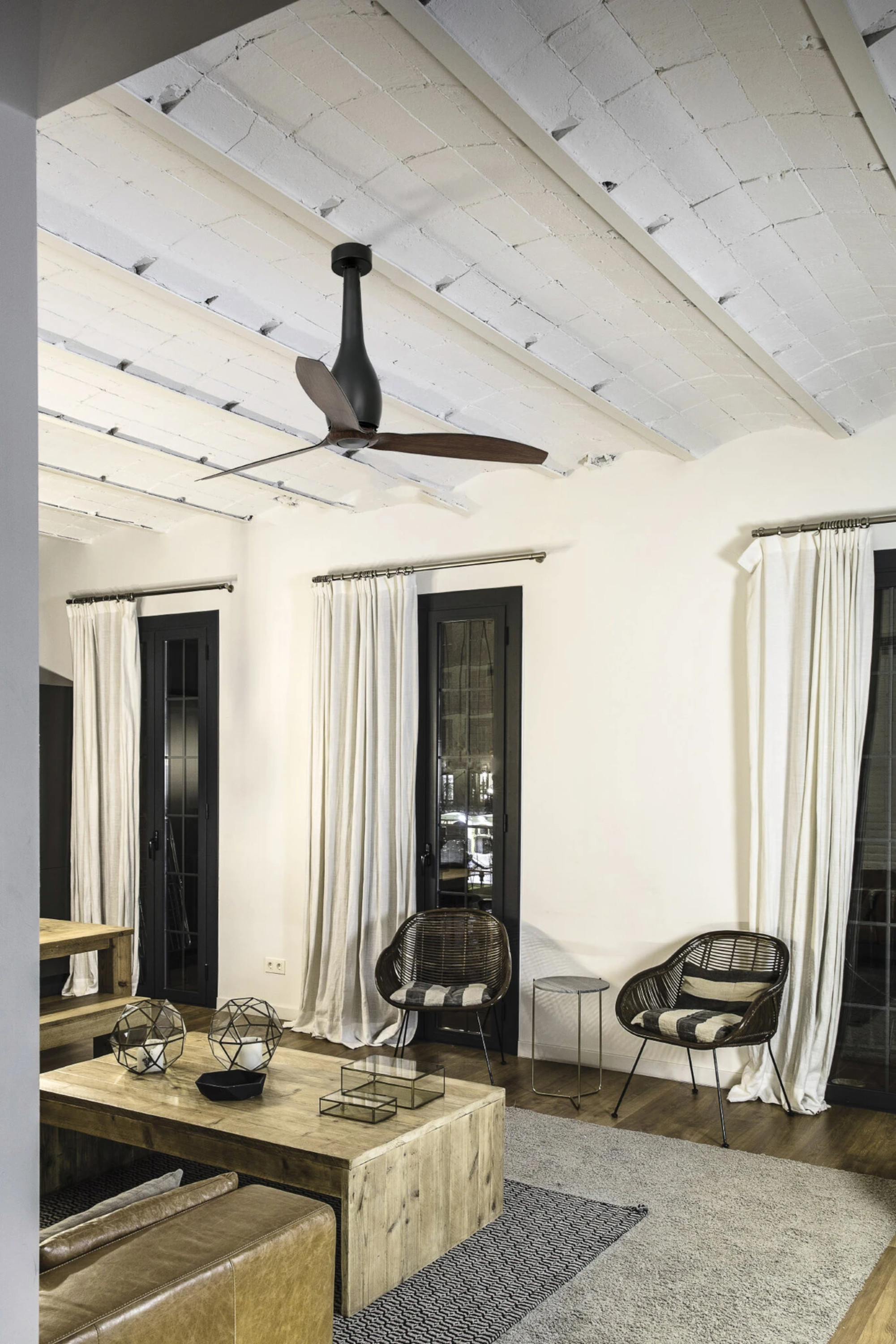 Ein modernes Wohnzimmer mit Deckenventilator, weißen Wänden und dunklen Türen.