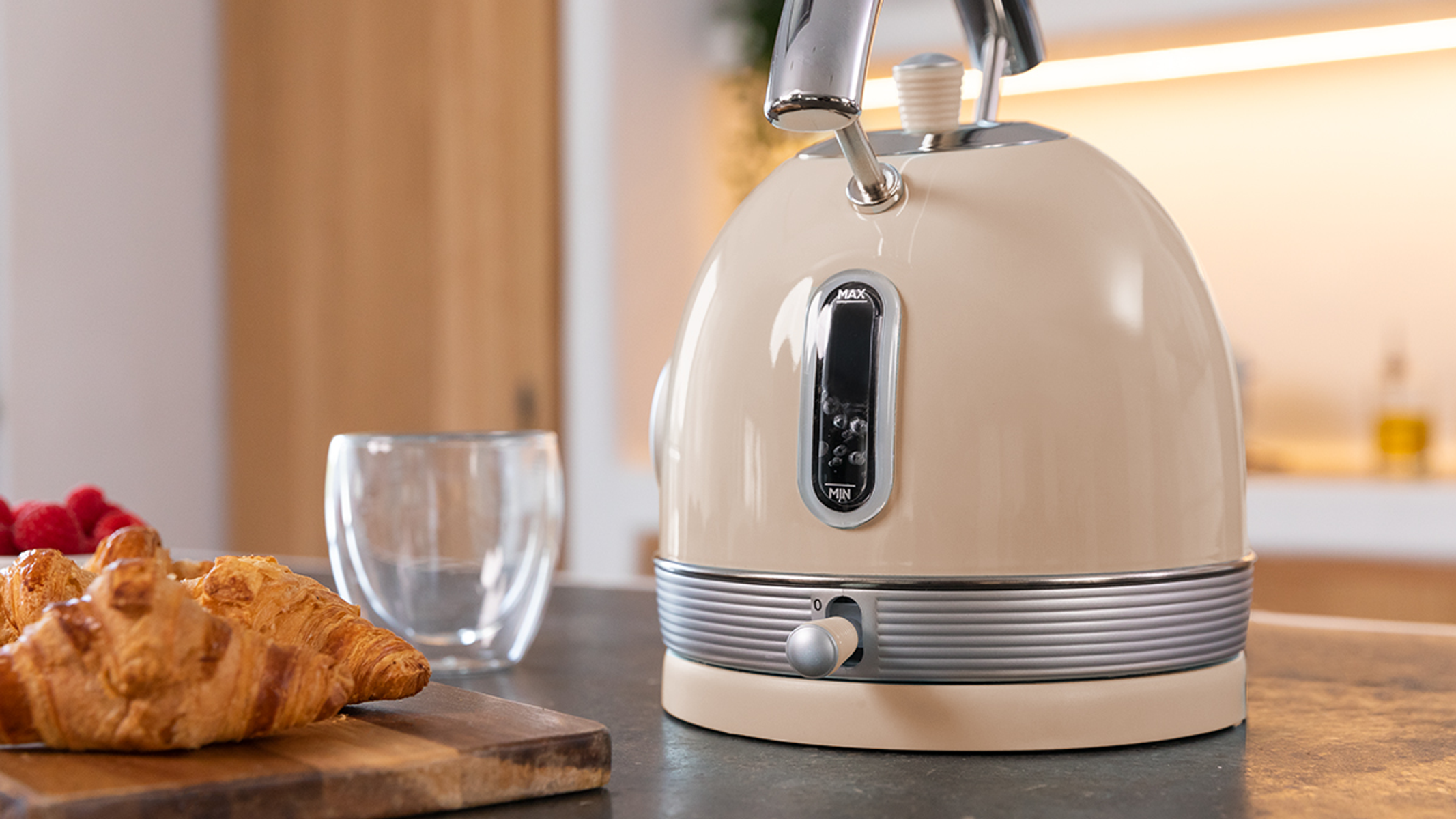 Beżowy czajnik elektryczny z rogalikami i szklanką na blacie.