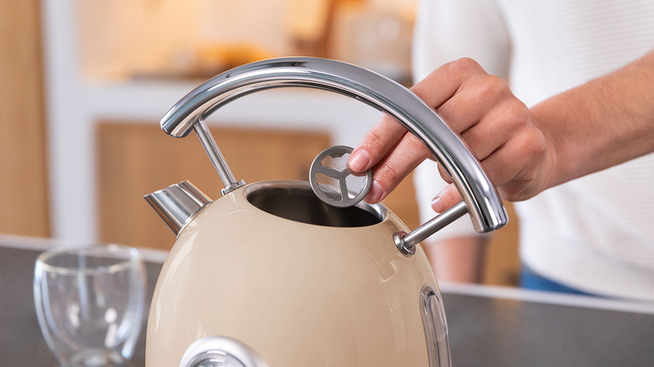 Ręka wkłada filtr do beżowego czajnika. Otoczenie kuchni.