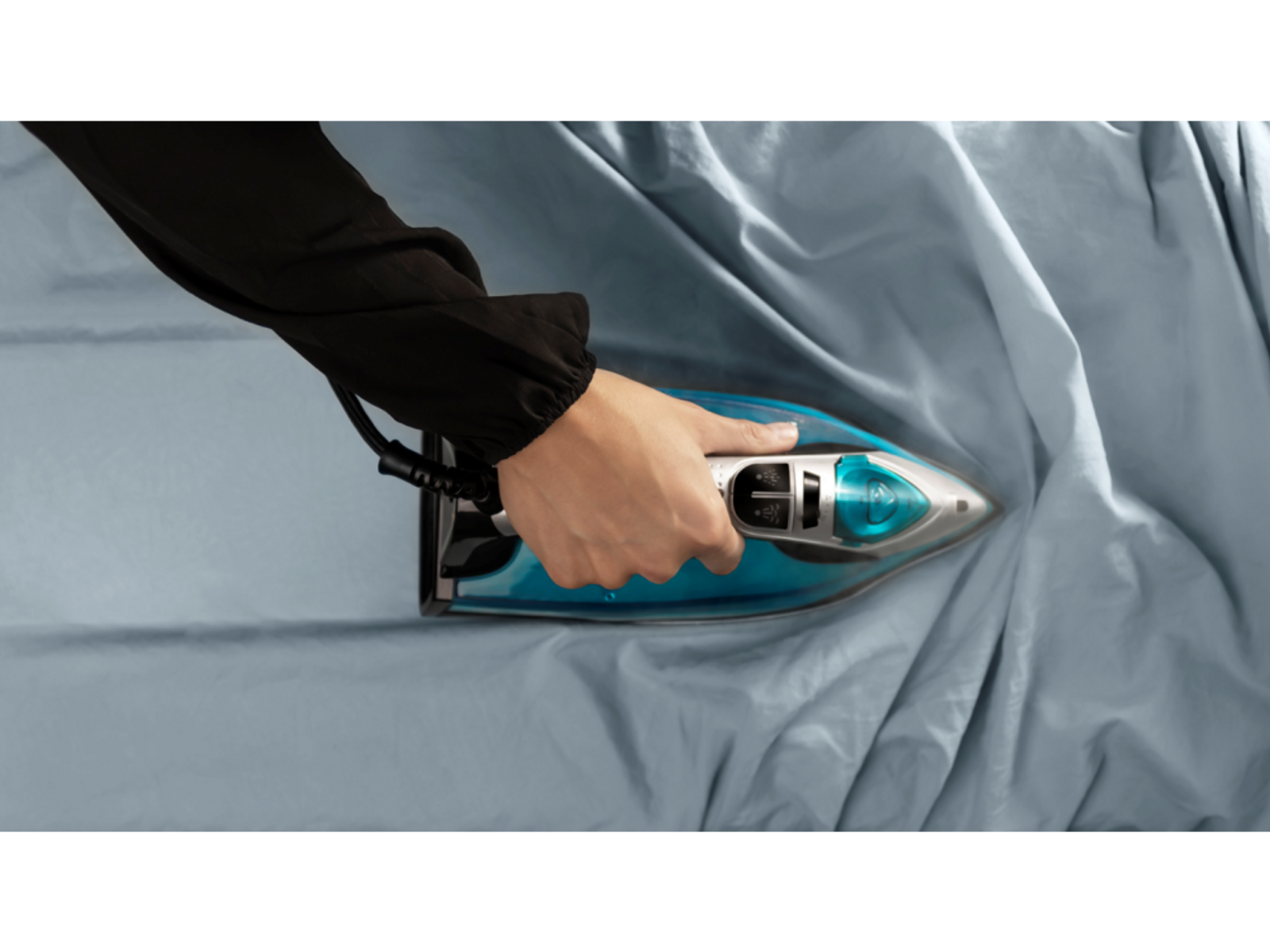Die Hand einer Person bügelt blauen Stoff mit einem blau-grauen Bügeleisen.
