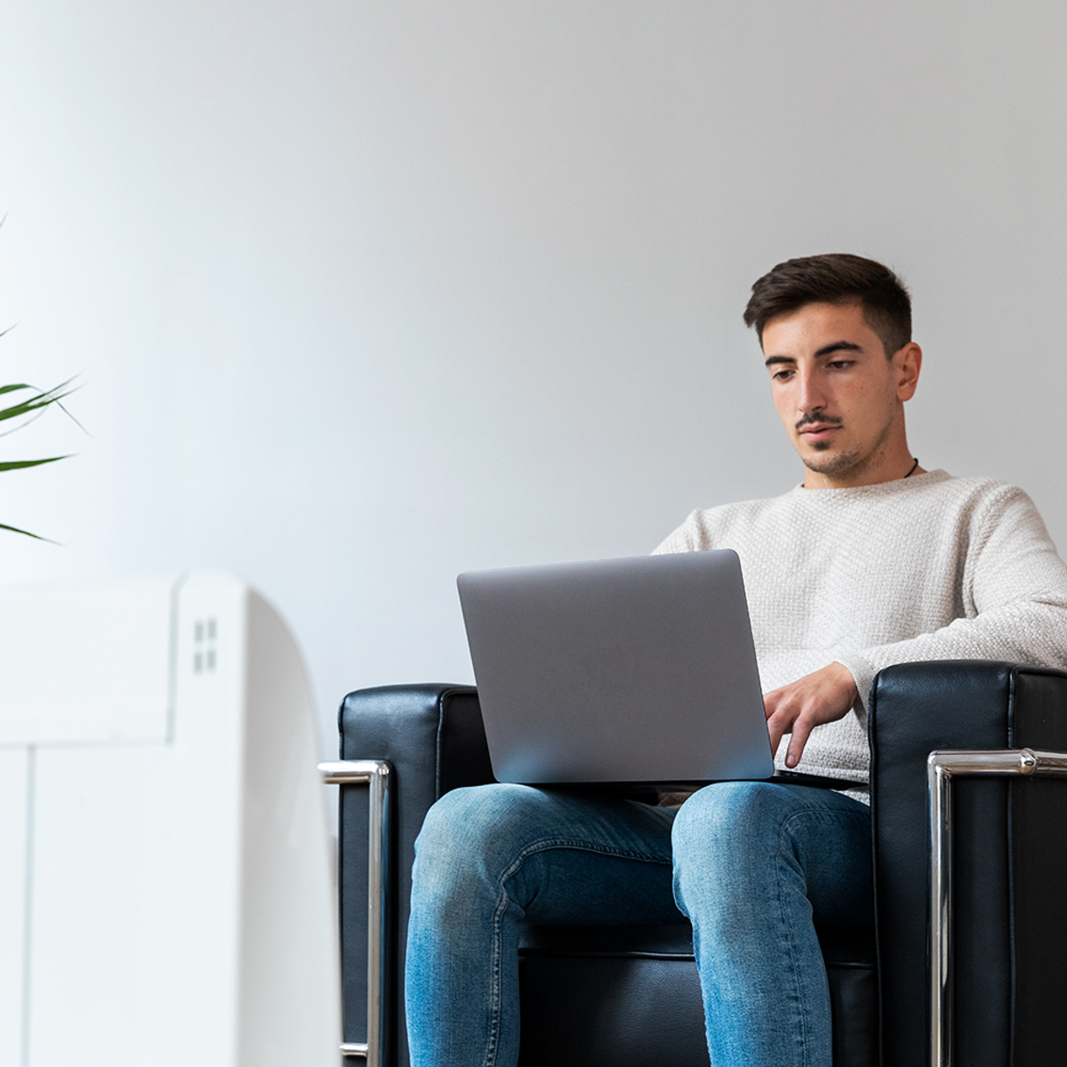 Mężczyzna z ciemnymi włosami siedzi na czarnym krześle, pracując na laptopie.
