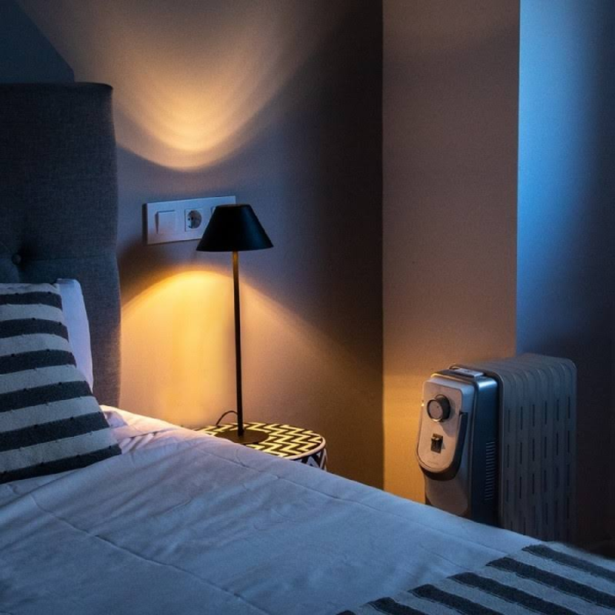 Scena sypialni z łóżkiem, lampą i grzejnikiem, rzucająca cienie.